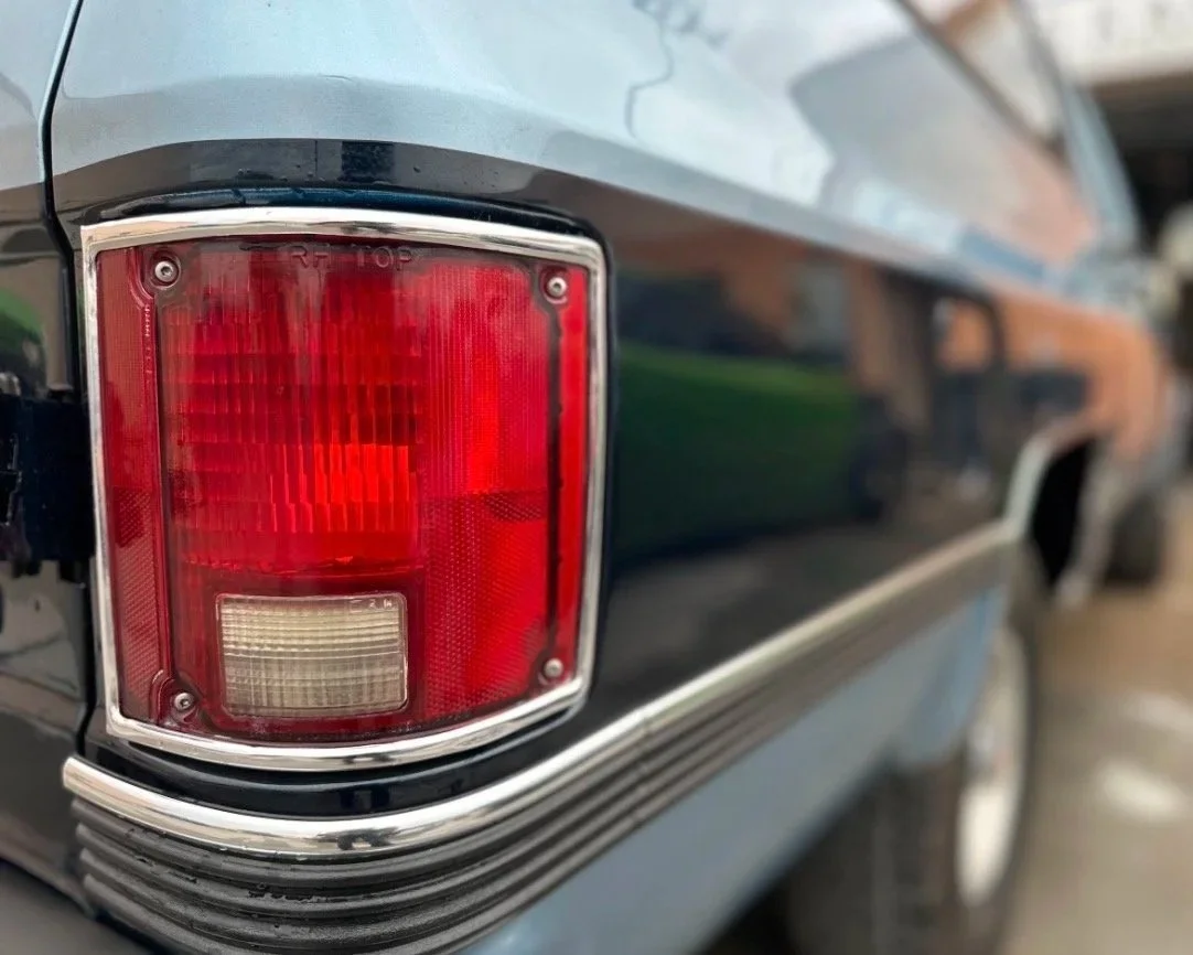 Close-up of a vintage car's red and chrome tail light with a chrome trim on a black body.