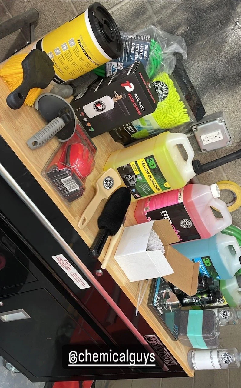 A wooden workbench with cleaning and industrial supplies, including bottles of degreasers, a brush, roller, scrapers, gloves, and various cleaning tools.
