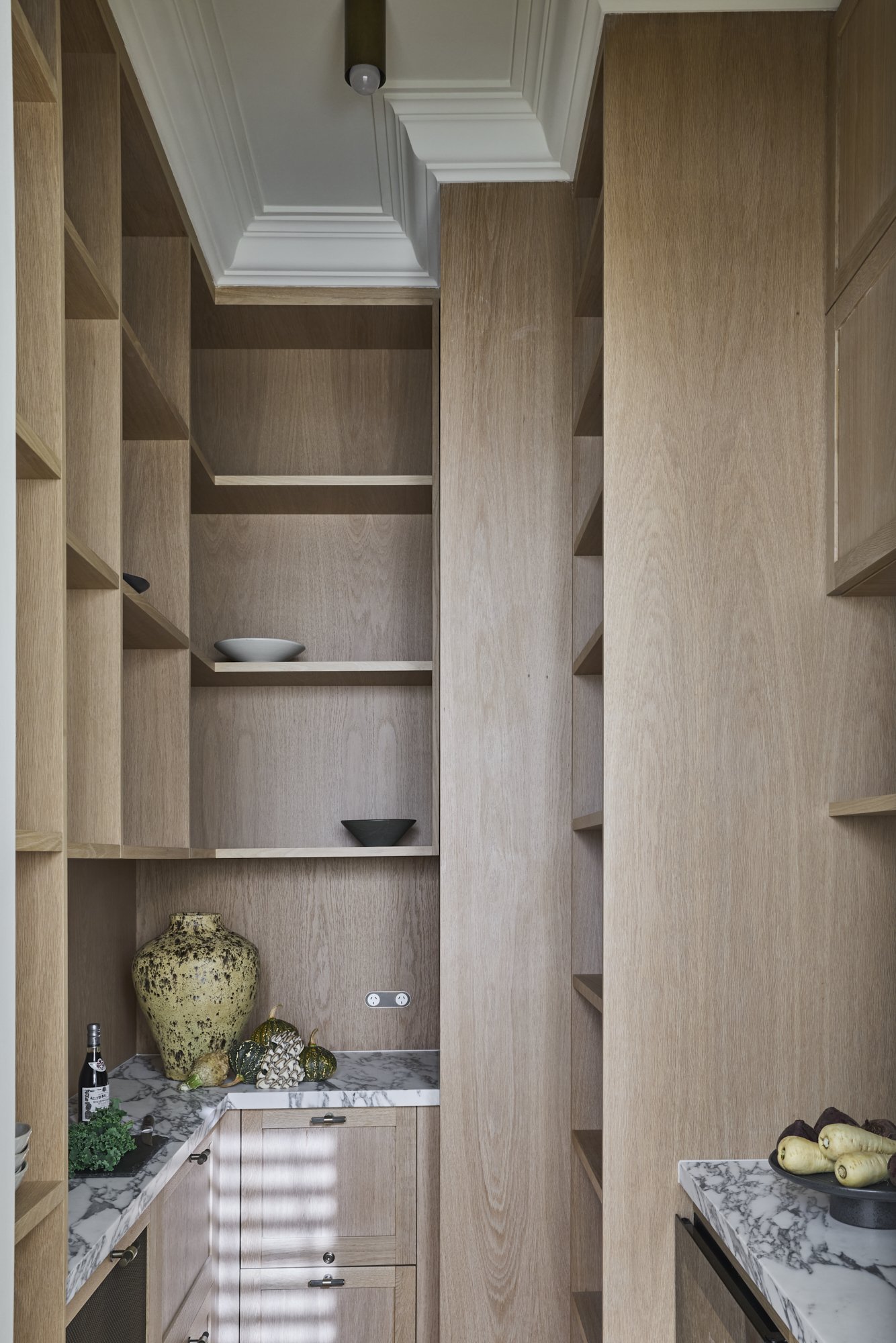 A walk-in pantry with wooden shelves and marble countertops, decorated with vases, bowls, and figurines.