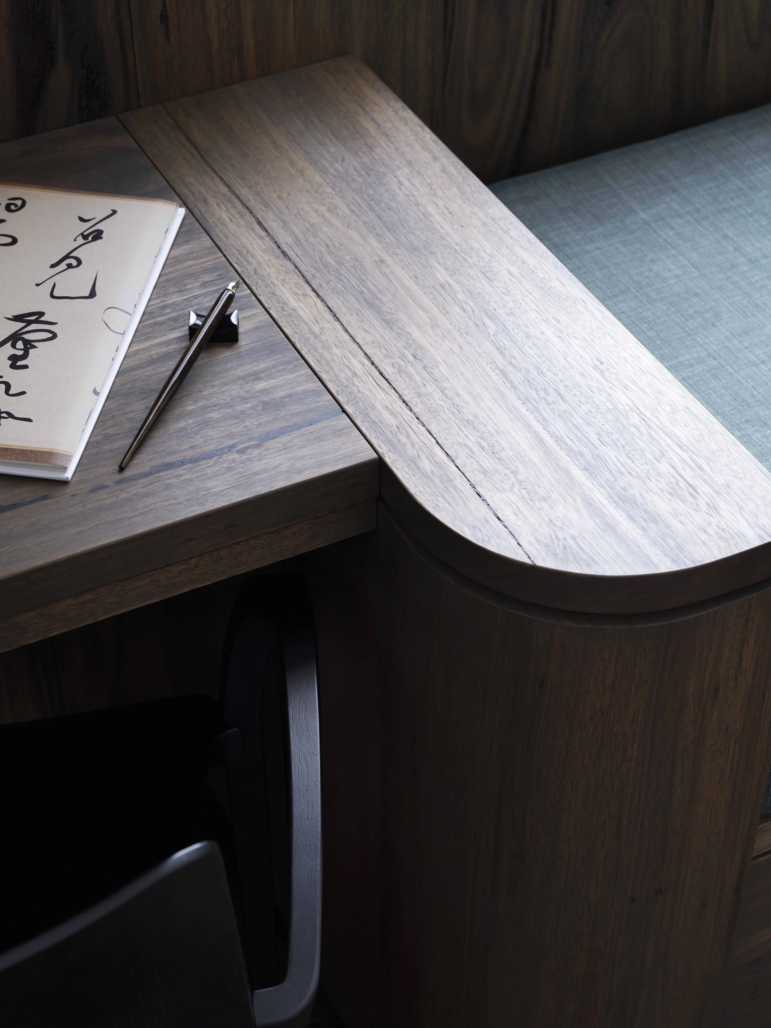 Close-up of a wooden desk with a calligraphy notebook and a metallic pen resting on it.