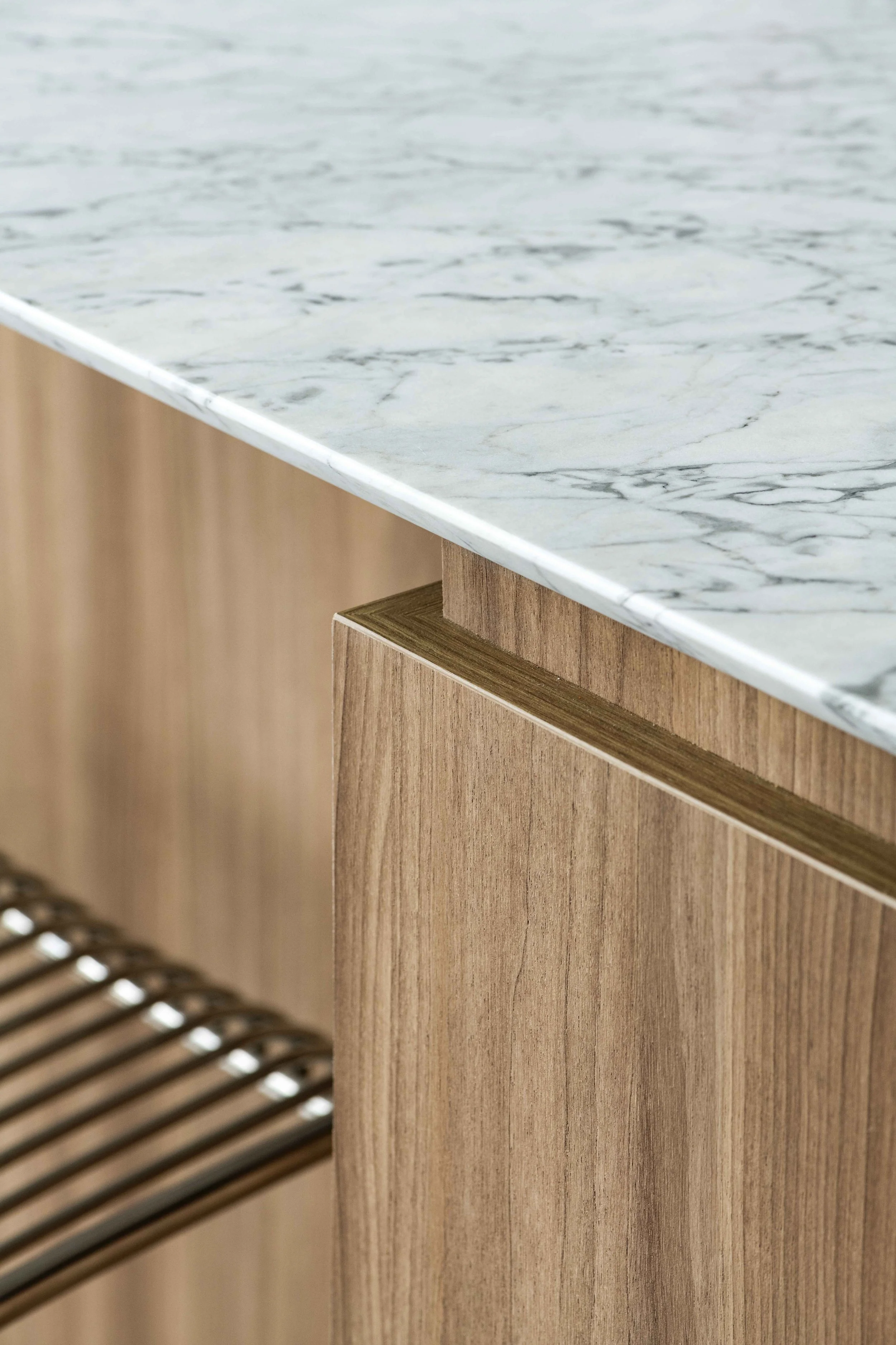 Close-up of a kitchen countertop with a marble surface and a wooden cabinet beneath it, showing part of a slatted wooden chair.