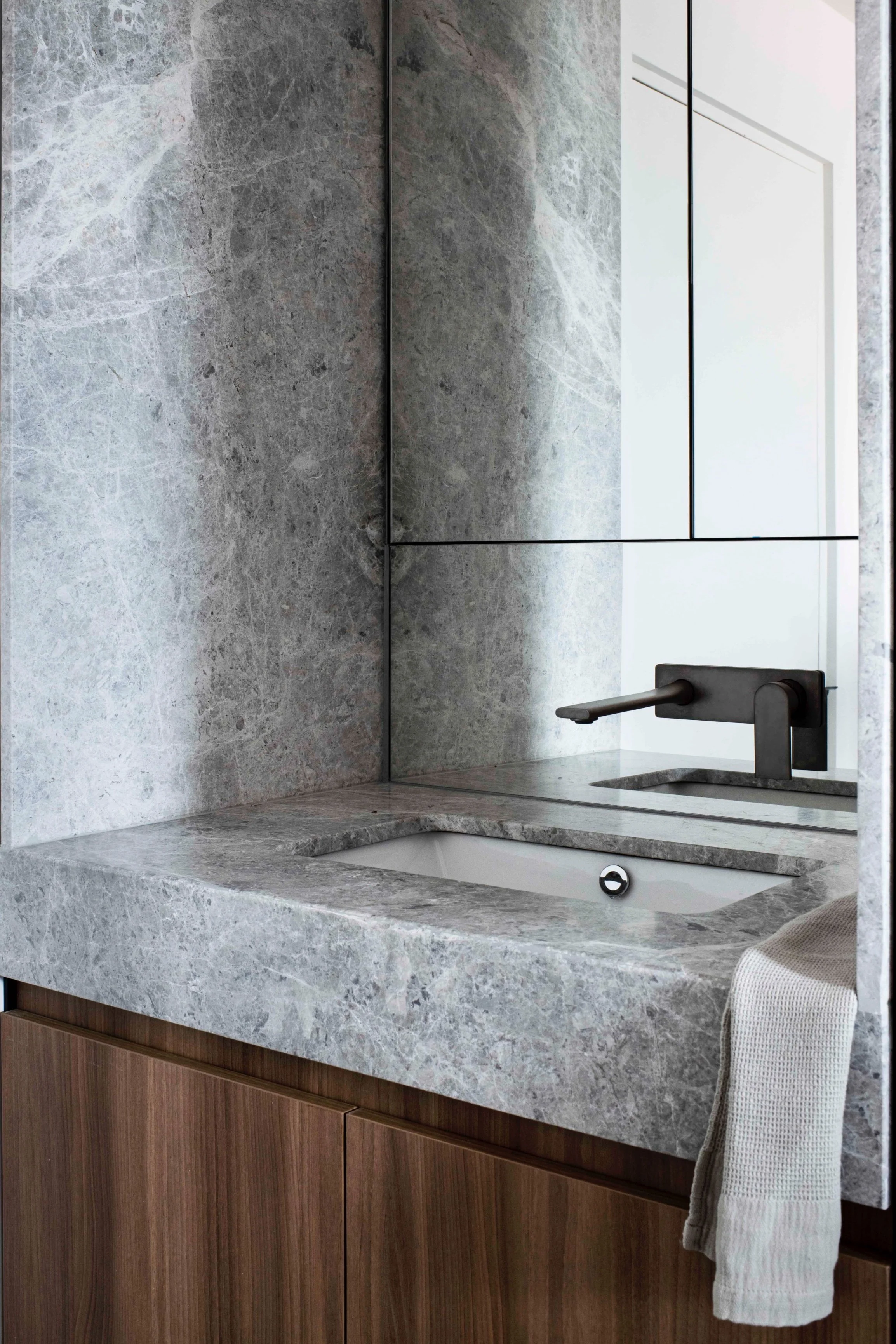 Modern bathroom with gray marble countertop and wall, rectangular sink, and black faucet, reflected in a mirror.