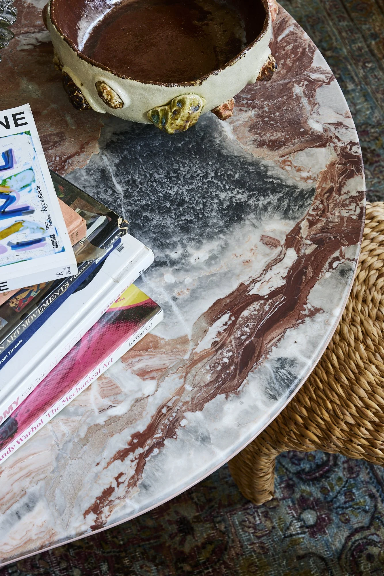 Coffee table with a marble pattern, a ceramic bowl, and a stack of books and magazines.