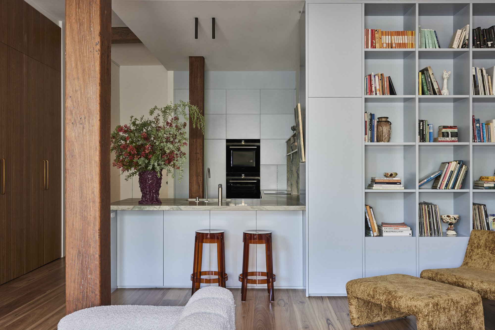 Modern kitchen with white cabinetry, a flower vase with red flowers, two orange chairs, and a large bookshelf filled with books