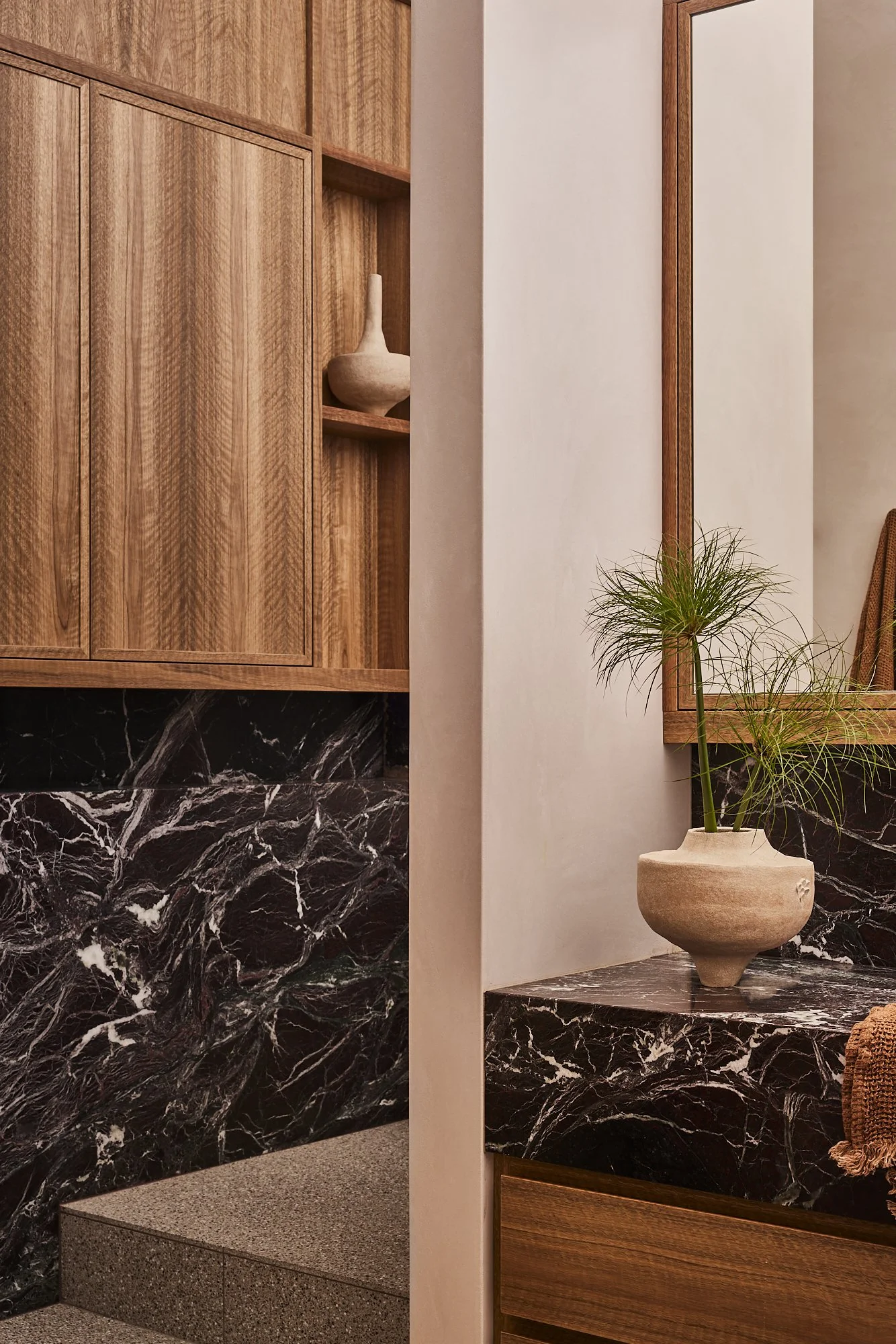 Interior space with wooden cabinets and black marble surfaces, decorated with a potted plant and a ceramic vase.