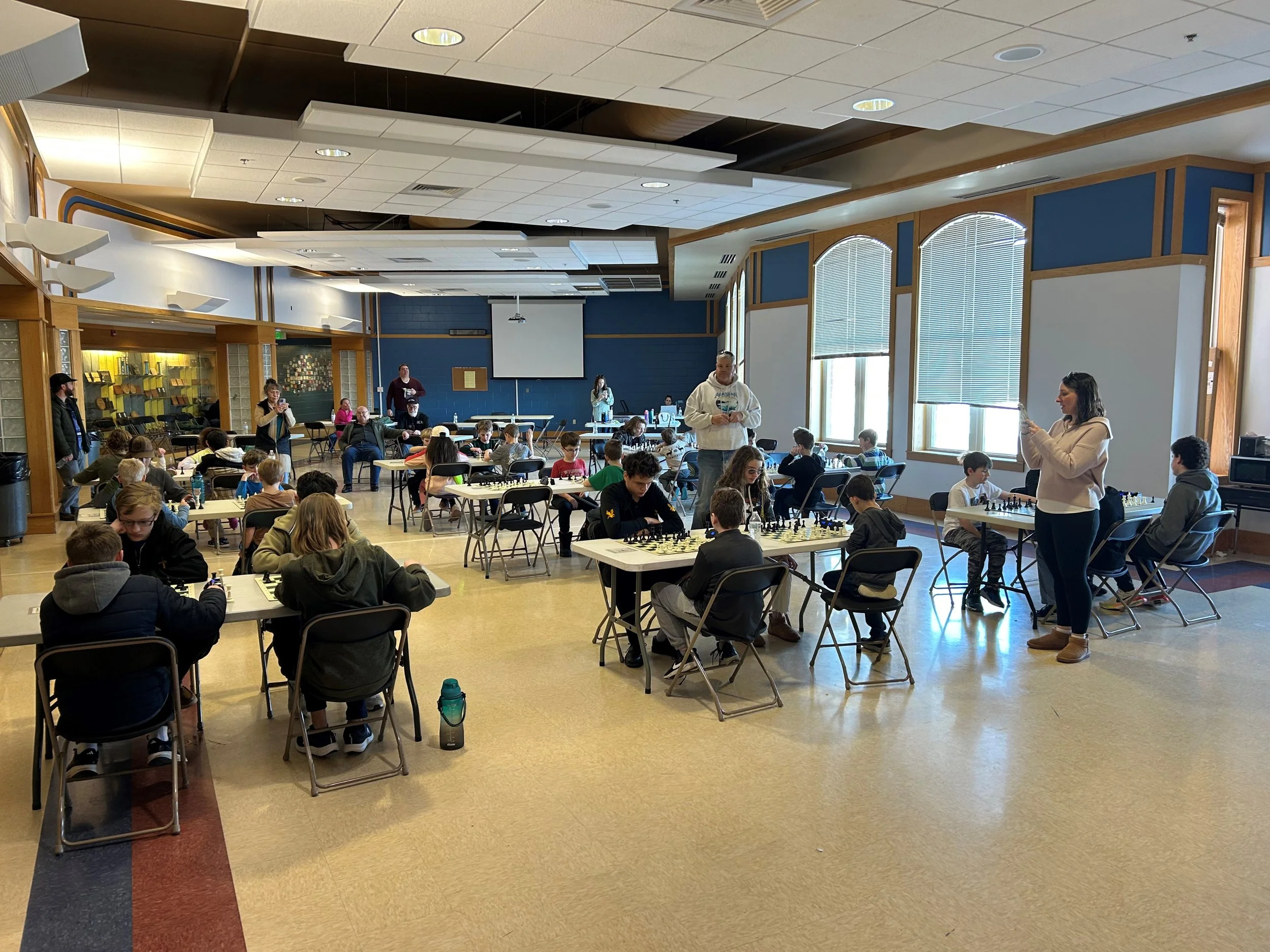People playing chess in a large room with tall windows, blue walls, and a high ceiling.