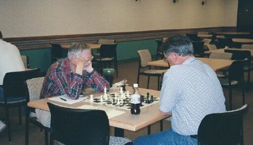 Two men playing chess in a dining area with empty tables and chairs.