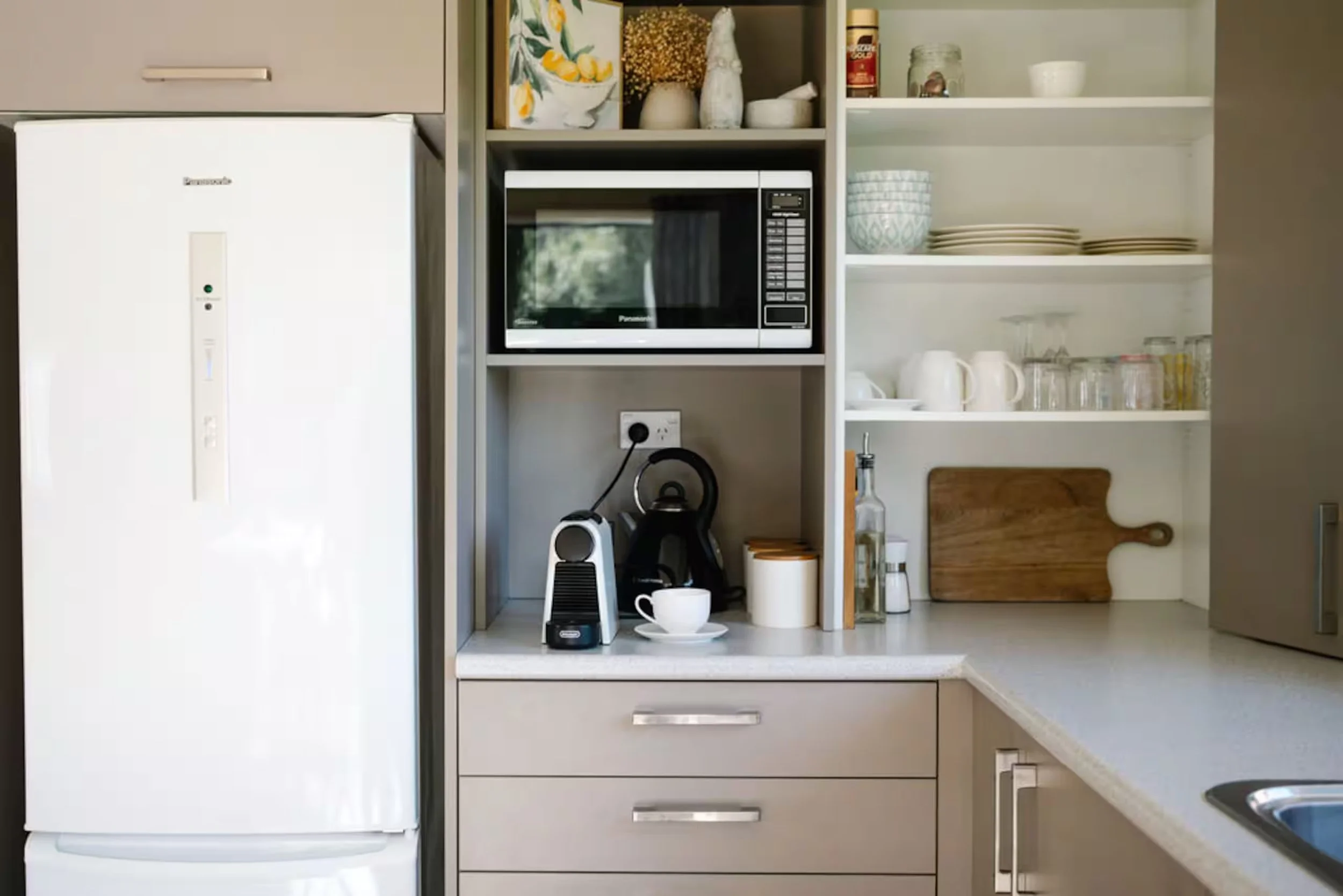 Modern kitchen with refrigerator, built-in microwave, coffee makers, open dish shelves, and wooden cutting boards