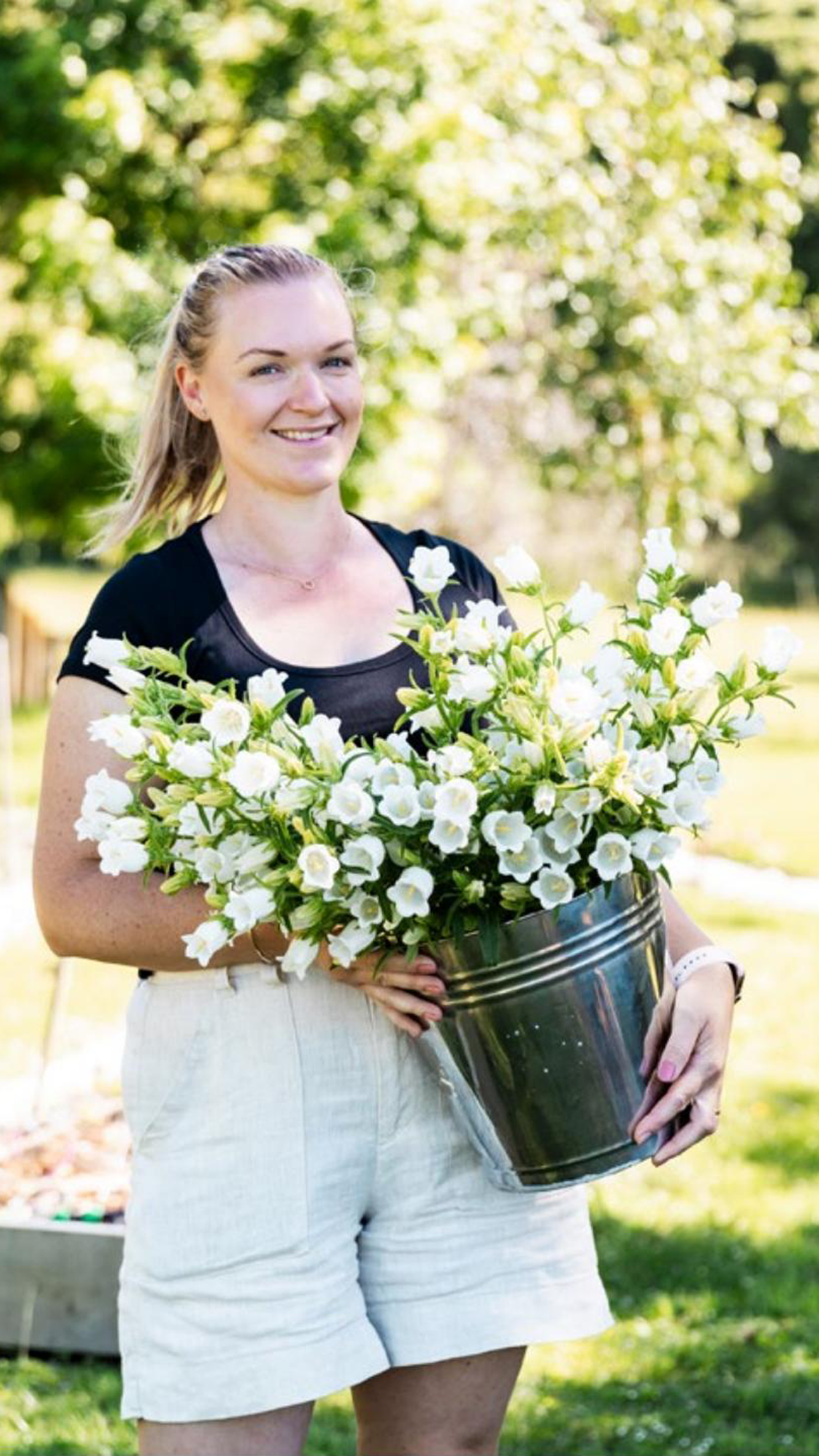 Woman smiling standing with a bucket of tall white flowers.
