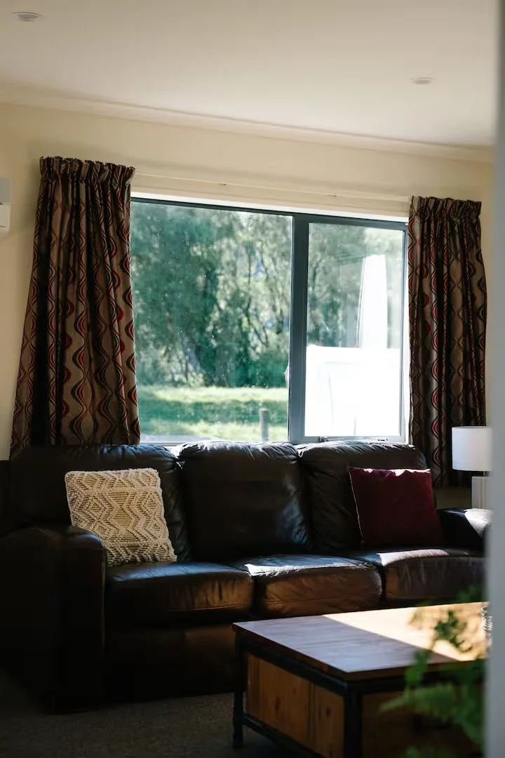 Cozy living room with a black leather sectional, patterned curtains, window, throw pillows, and wooden coffee table