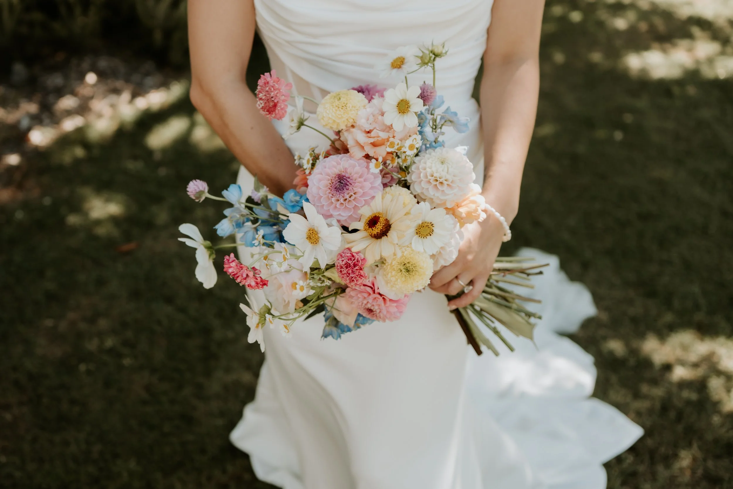 Bride in a white wedding dress holding a colorful wildflower bouquet outdoors