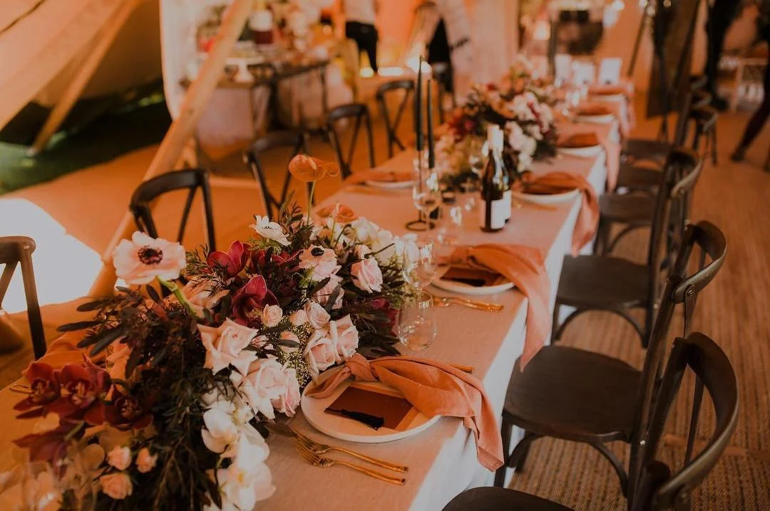 Elegant wedding reception tablescape with floral centerpiece, peach napkins, place settings, candles, and wine bottles