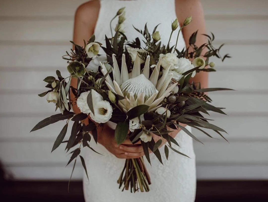 Bride in a white dress holding a large white protea and greenery wedding bouquet