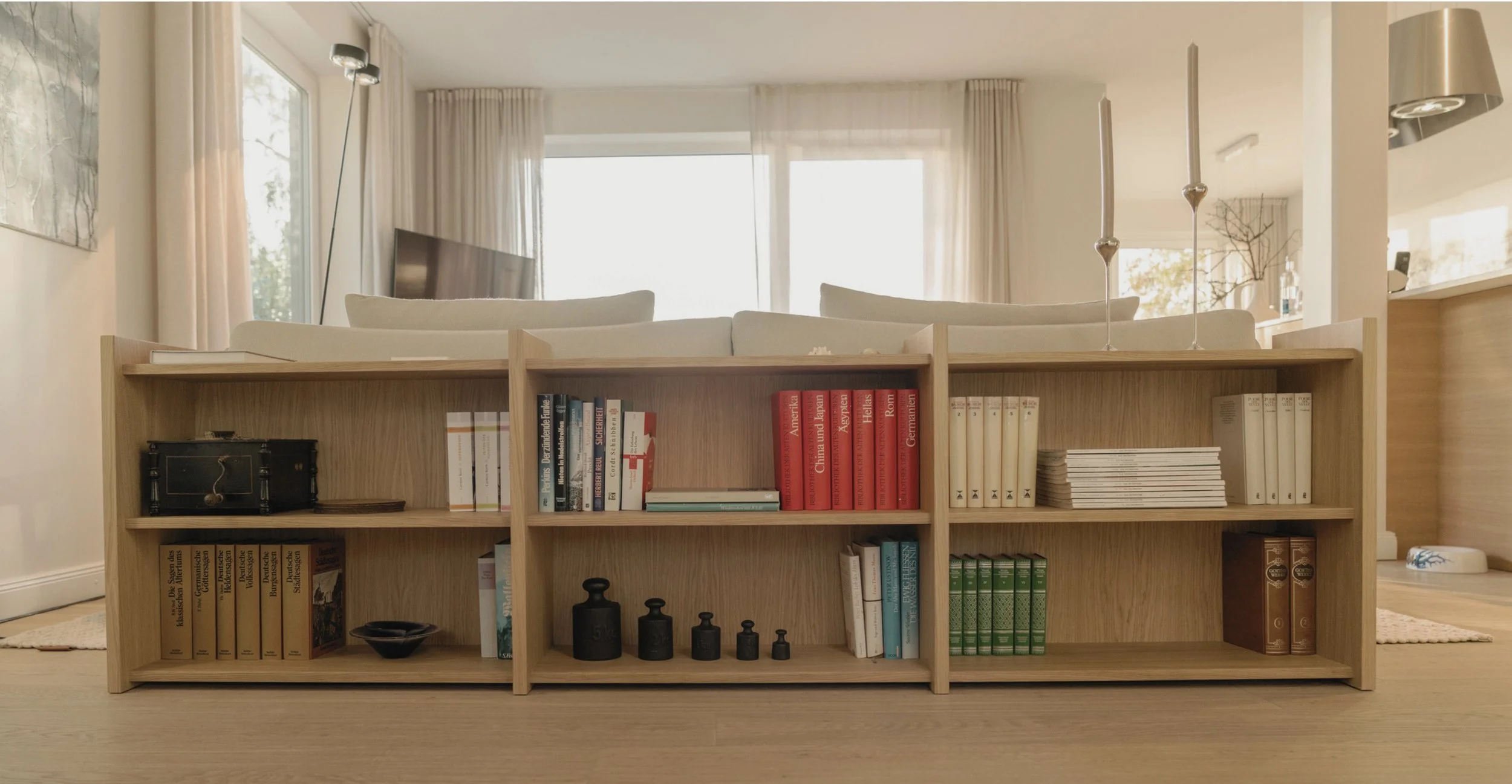 Maßbefertigtes Regal hinter einem Sofa. Das Sofa grenzt den Wohnbereich ab.