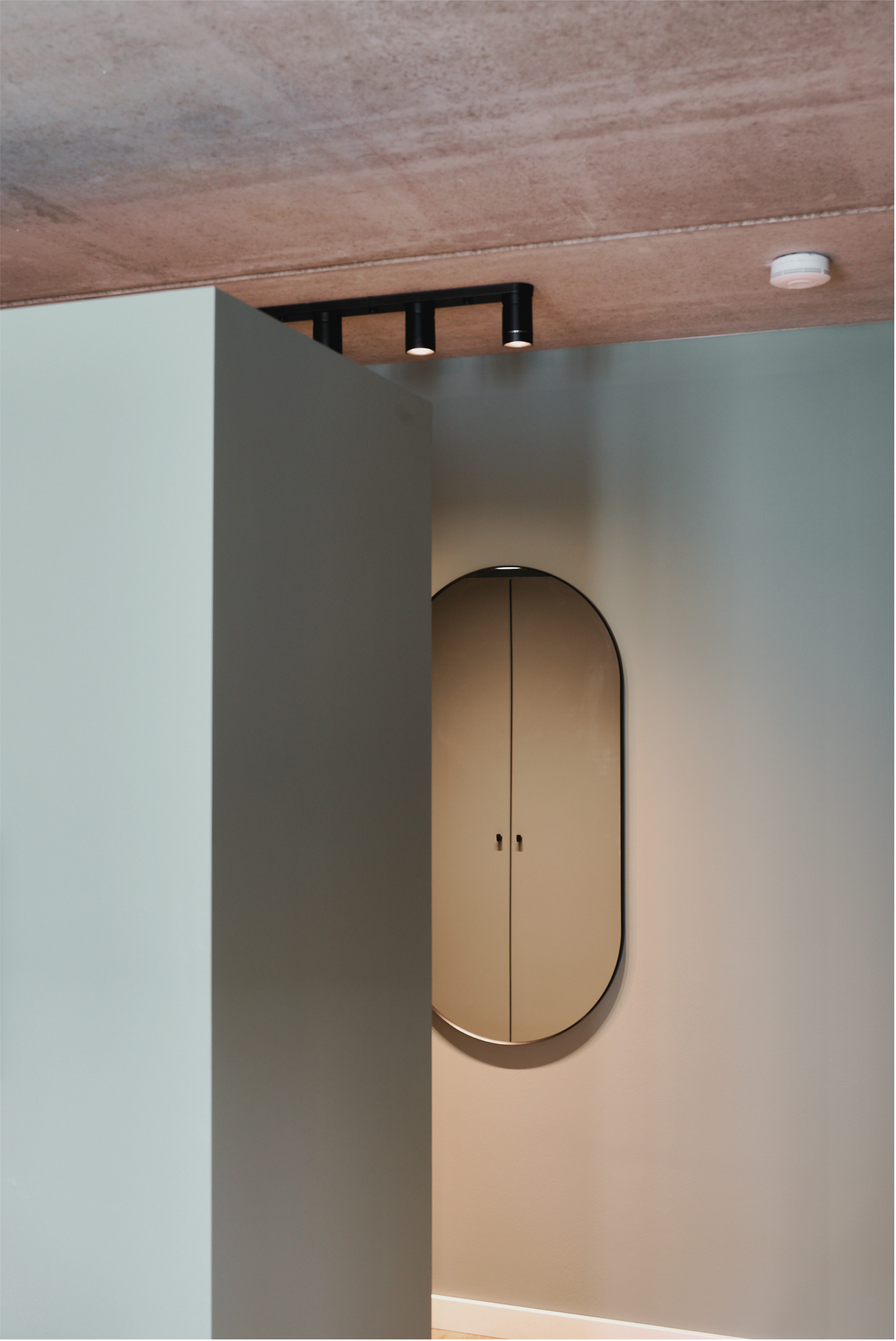 Innenraum der Musterwohnung mit grünen Wänden, ovalem Spiegel und Sichtbetondecke.