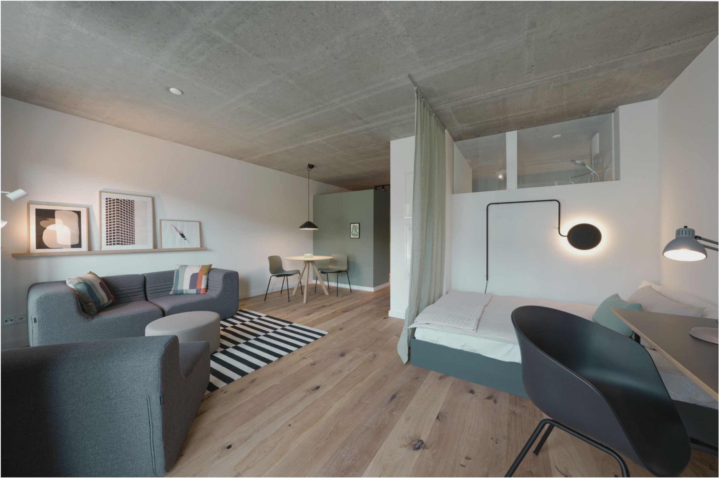 Offene, modern eingerichtete Wohnung mit Wohnzimmer, Essbereich, Schlafzimmer und Obergeschoss mit Dusche, hohe Decke, bohlenholzboden, Kunstwerken an der Wand, Möbel in neutralen Farben, Beleuchtung, Vorhang und Blick auf den lichtdurchfluteten Raum.