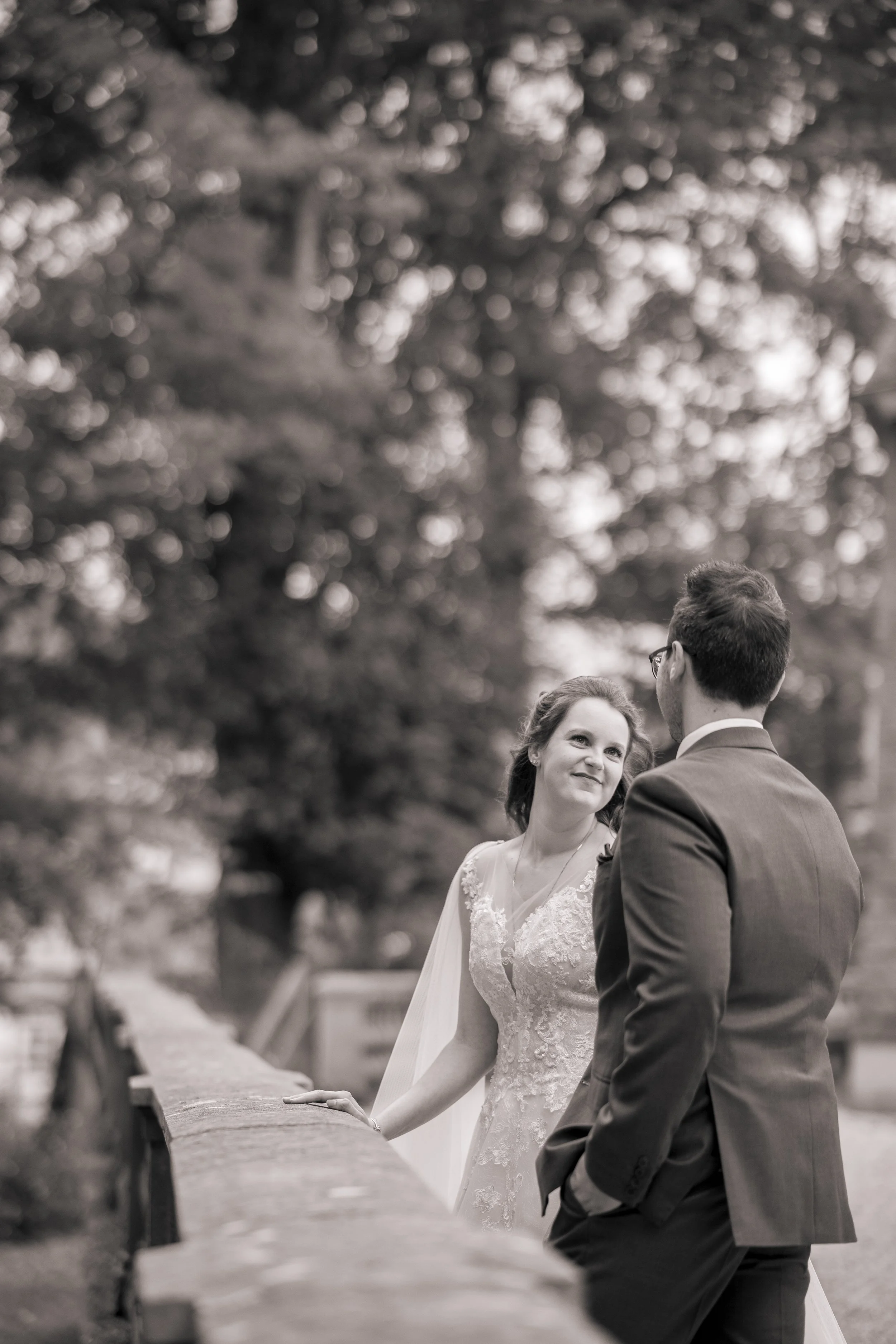 Ein Brautpaar bei ihrer Hochzeit im Freien, im Gespräch, im Hintergrund Bäume, in Schwarz-Weiß gehalten.