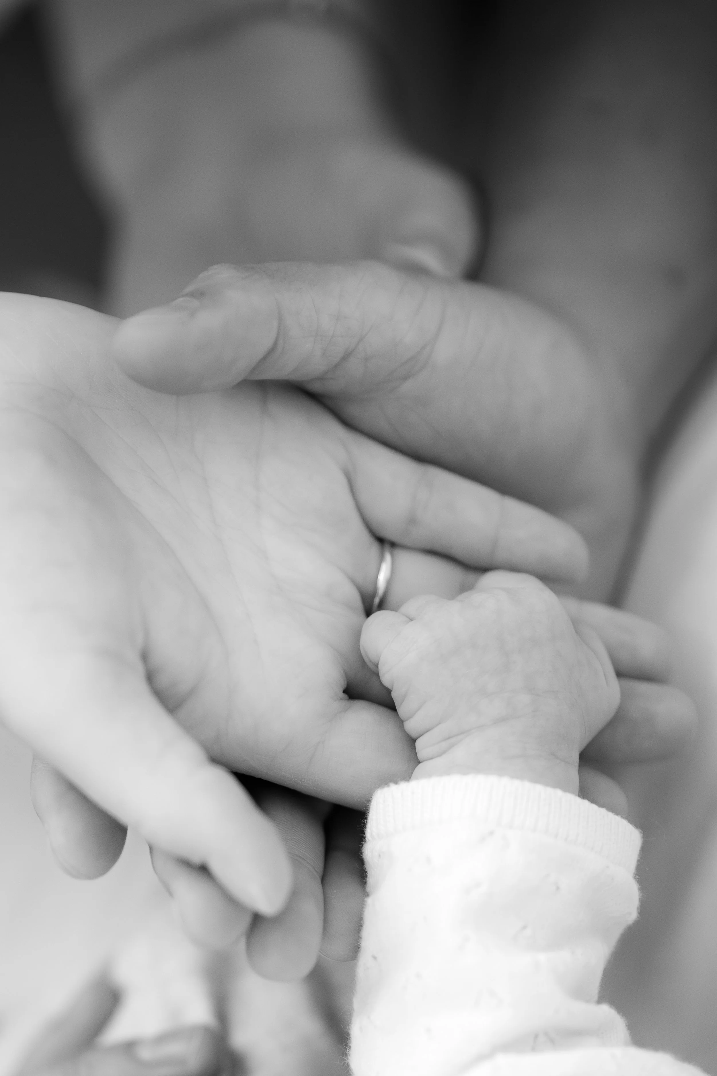 Nahaufnahme von einer Hand, die eine kleine Babyhand hält, in Schwarz-Weiß.