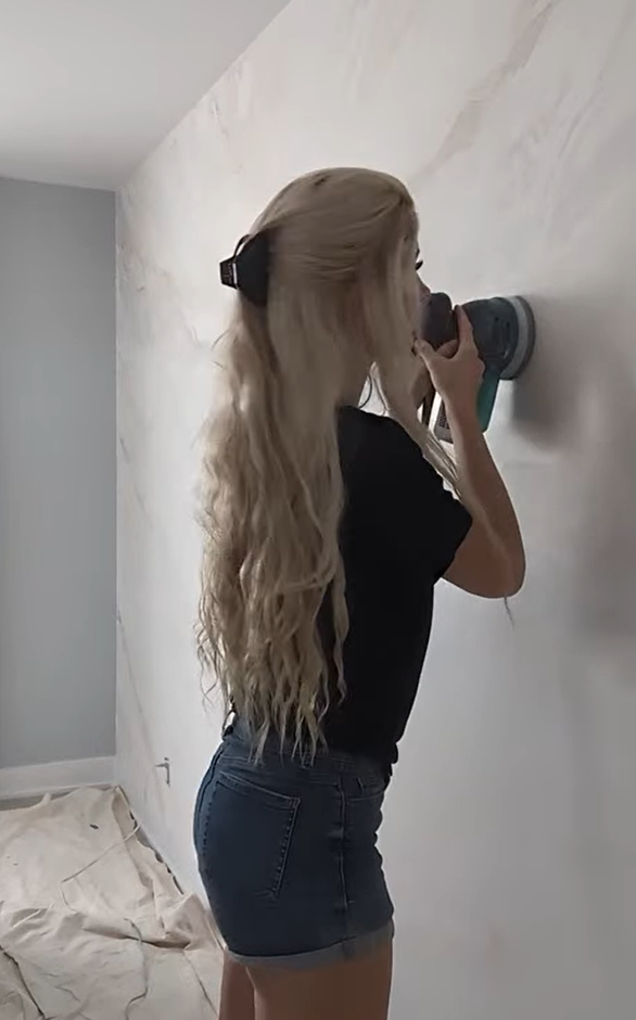 Jeune femme blonde utilisant une ponceuse murale dans une pièce en rénovation.
