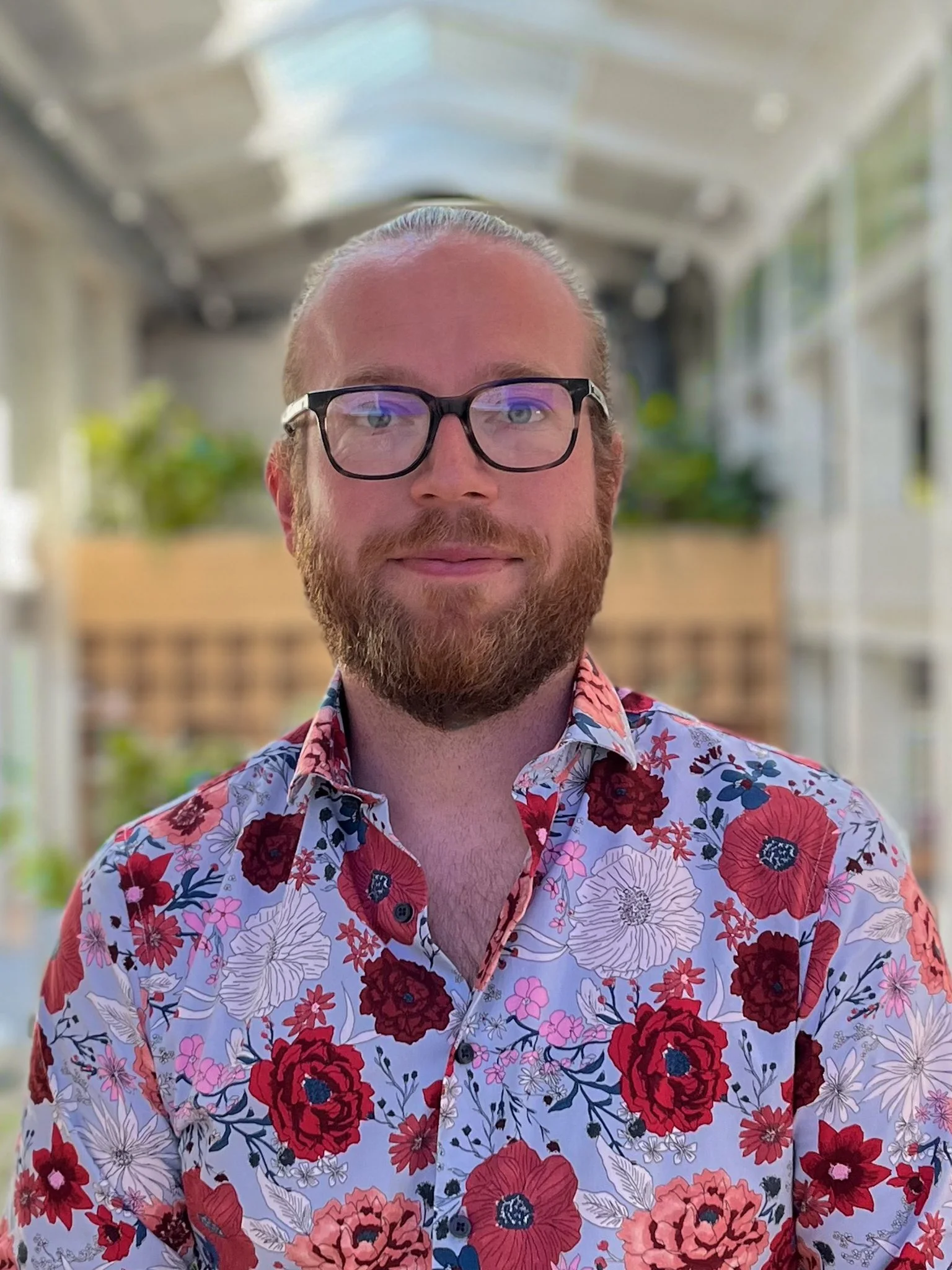 Man met rood haar, bril en een baard, draagt een bloemenoverhemd.