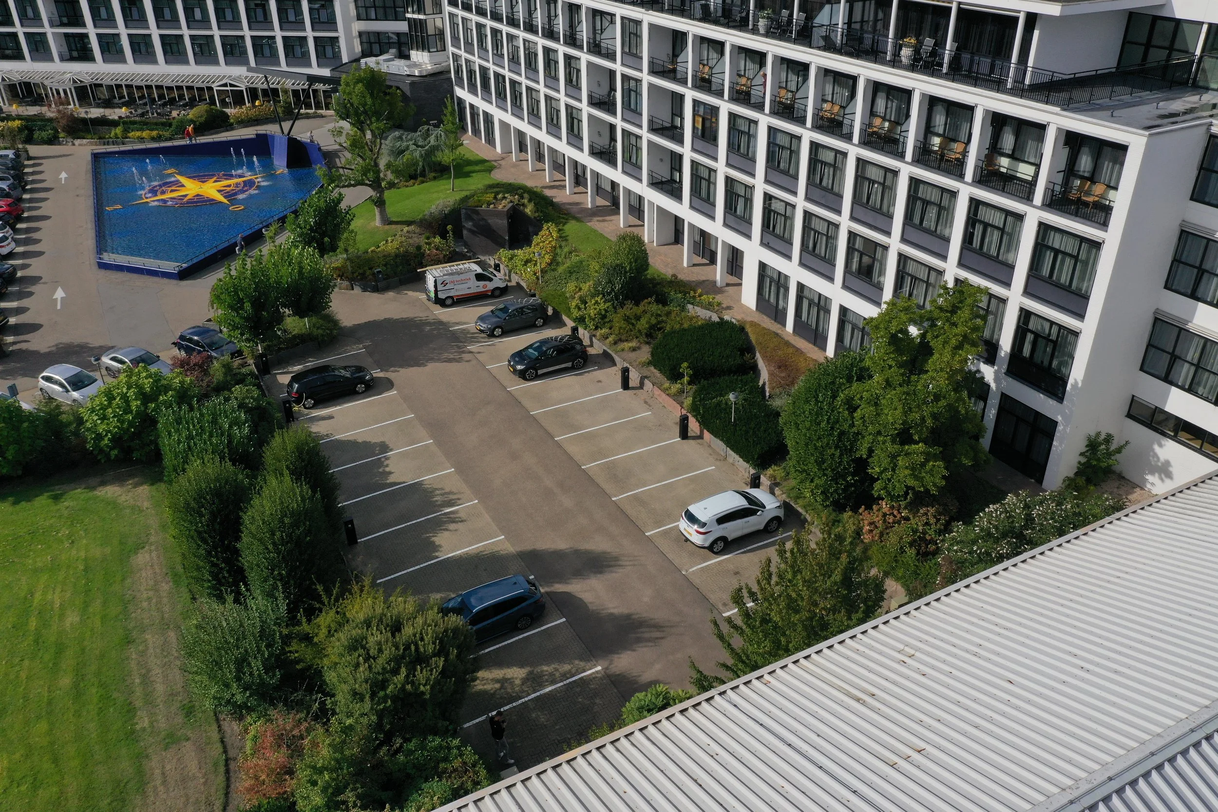 Hoogwaardige fotografische opname van een modern appartementencomplex met een zwembad en een parkeerplaats onder helder daglicht.