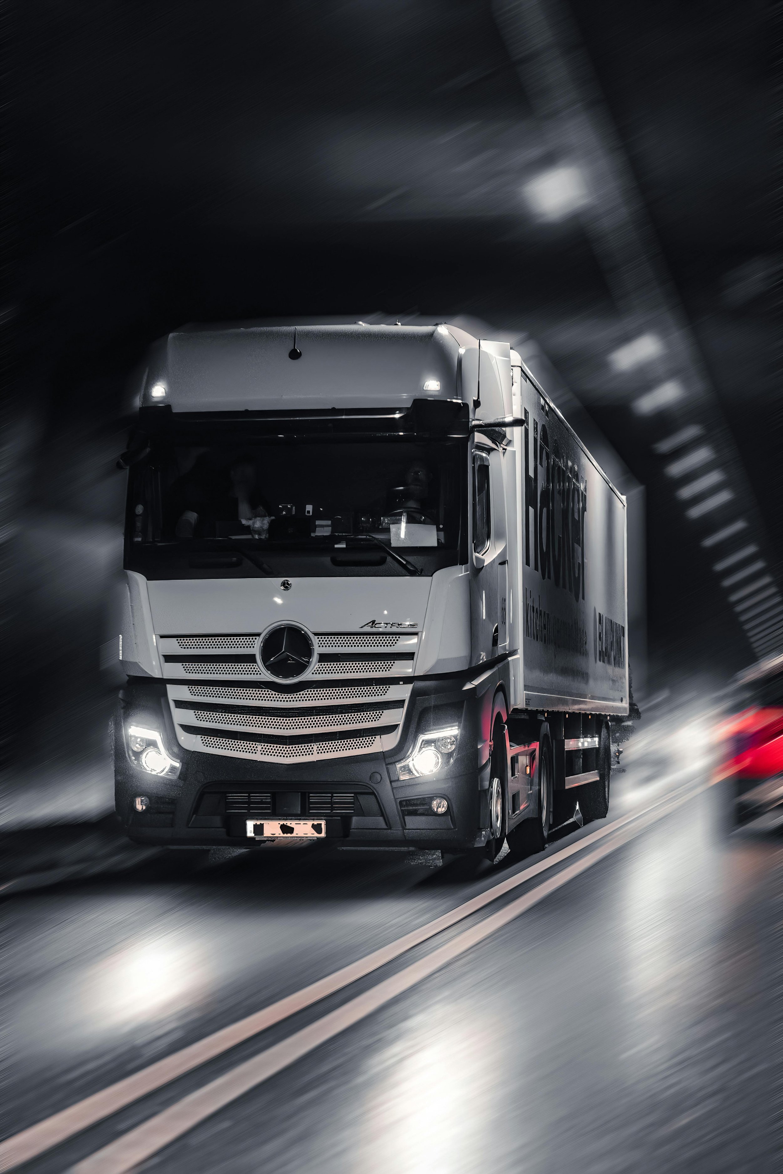 Een Mercedes-Benz vrachtwagen rijdt door een donkere tunnel met snel bewegende lichtvlekken op de achtergrond.