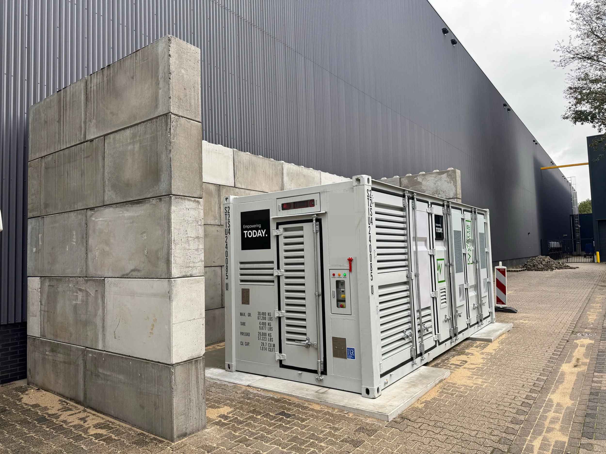 Een moderne industriebouw met metalen gevel en een grote container met technische inrichting op de voorgrond.