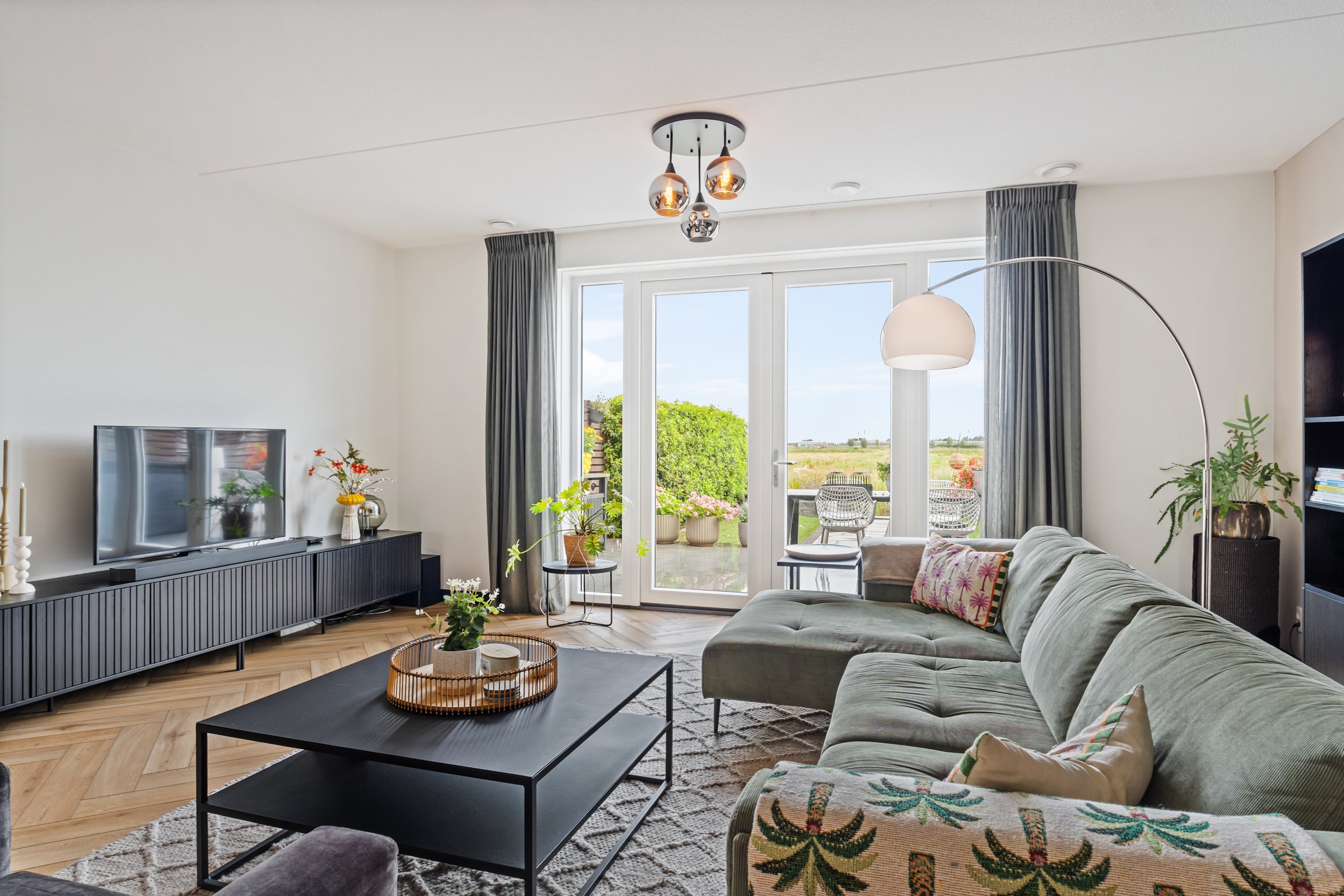 Woonkamer met bank, salontafel, tv, planten, en uitzicht op een tuin met terras.