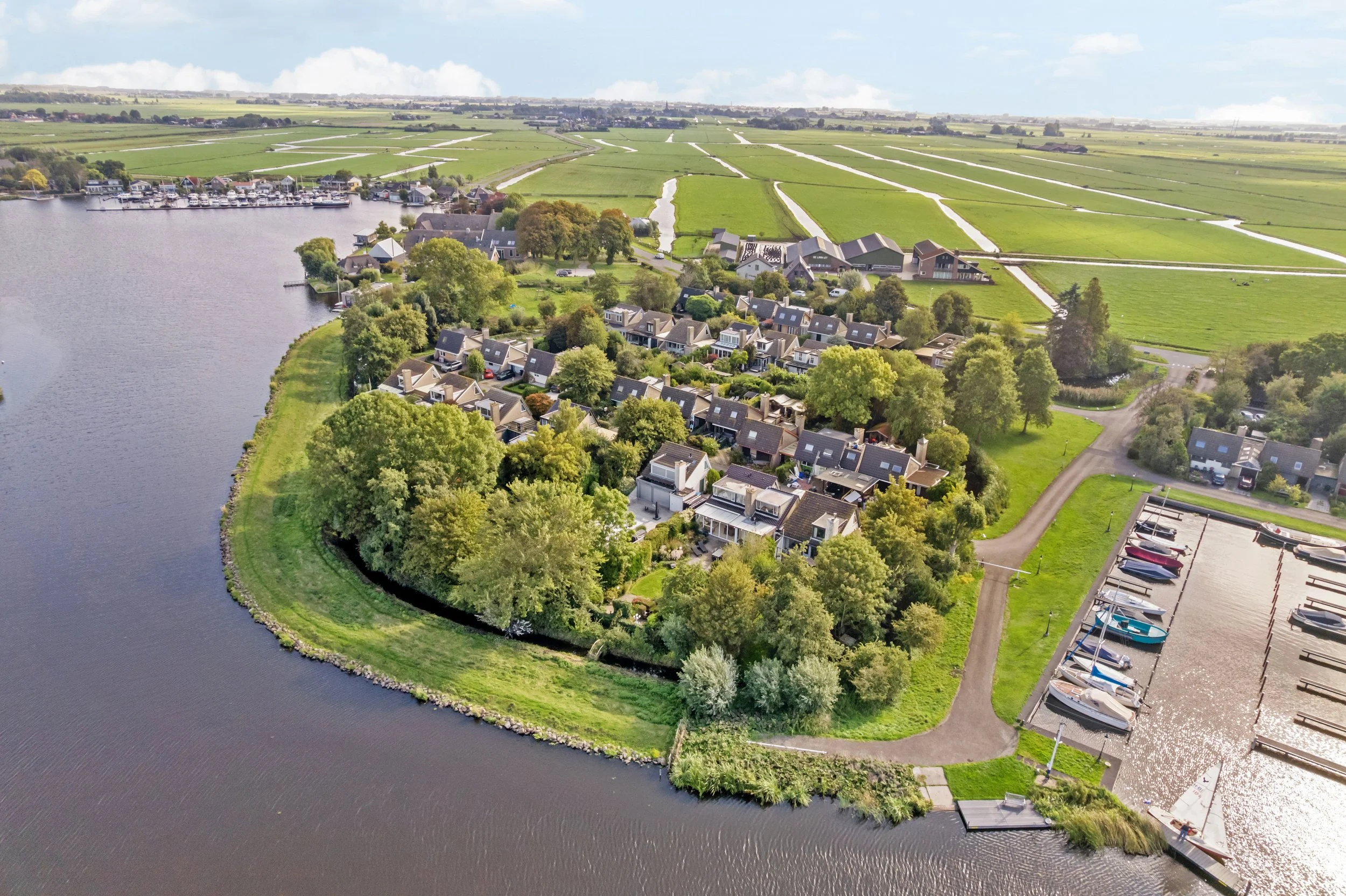 Luchtfoto van een rustig dorp aan een rivier met een haven en omliggende groene velden.