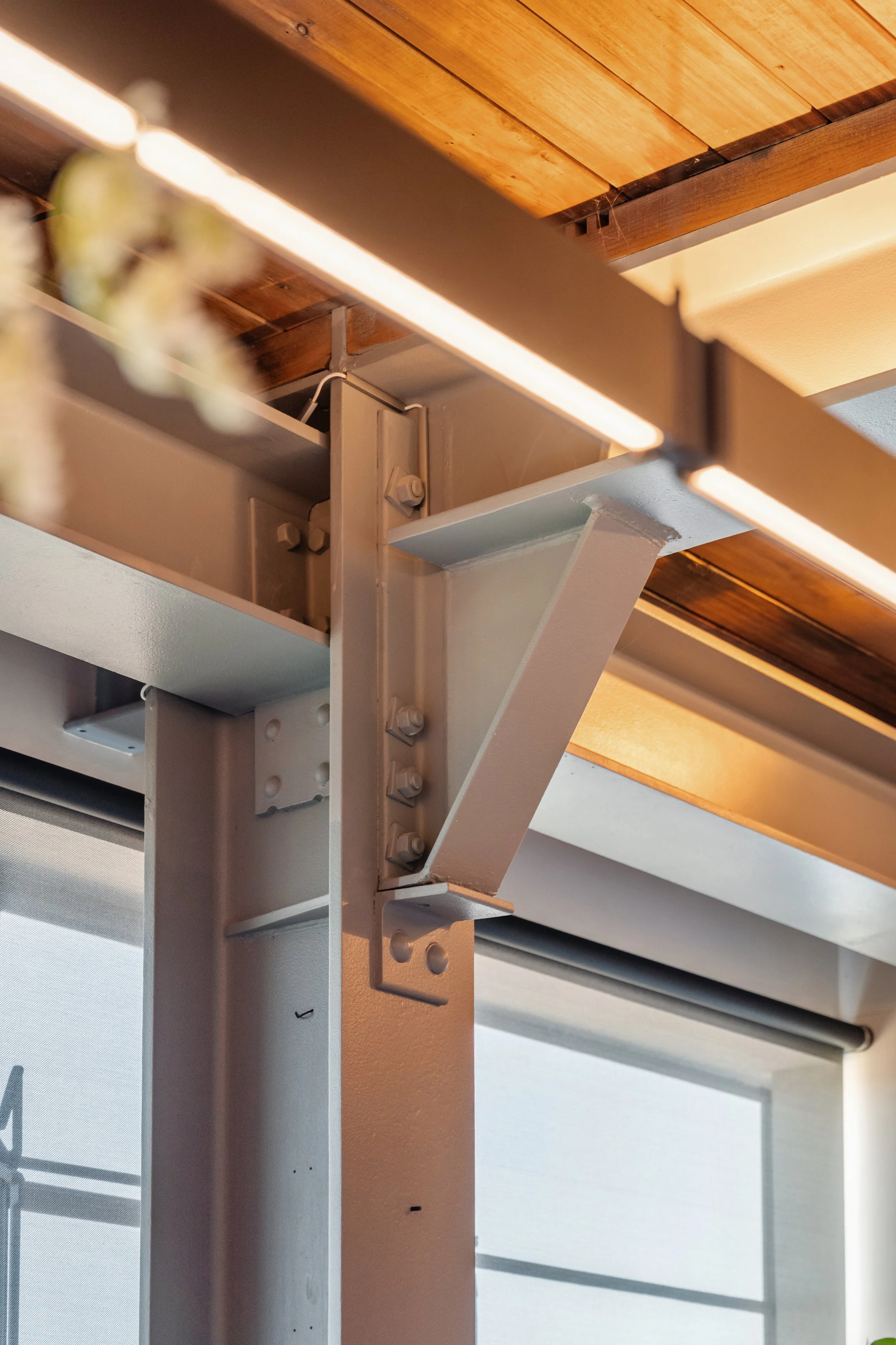 Close-up van een metalen constructie onder een houten plafond, met zicht op schroeven en bevestigingsmaterialen.