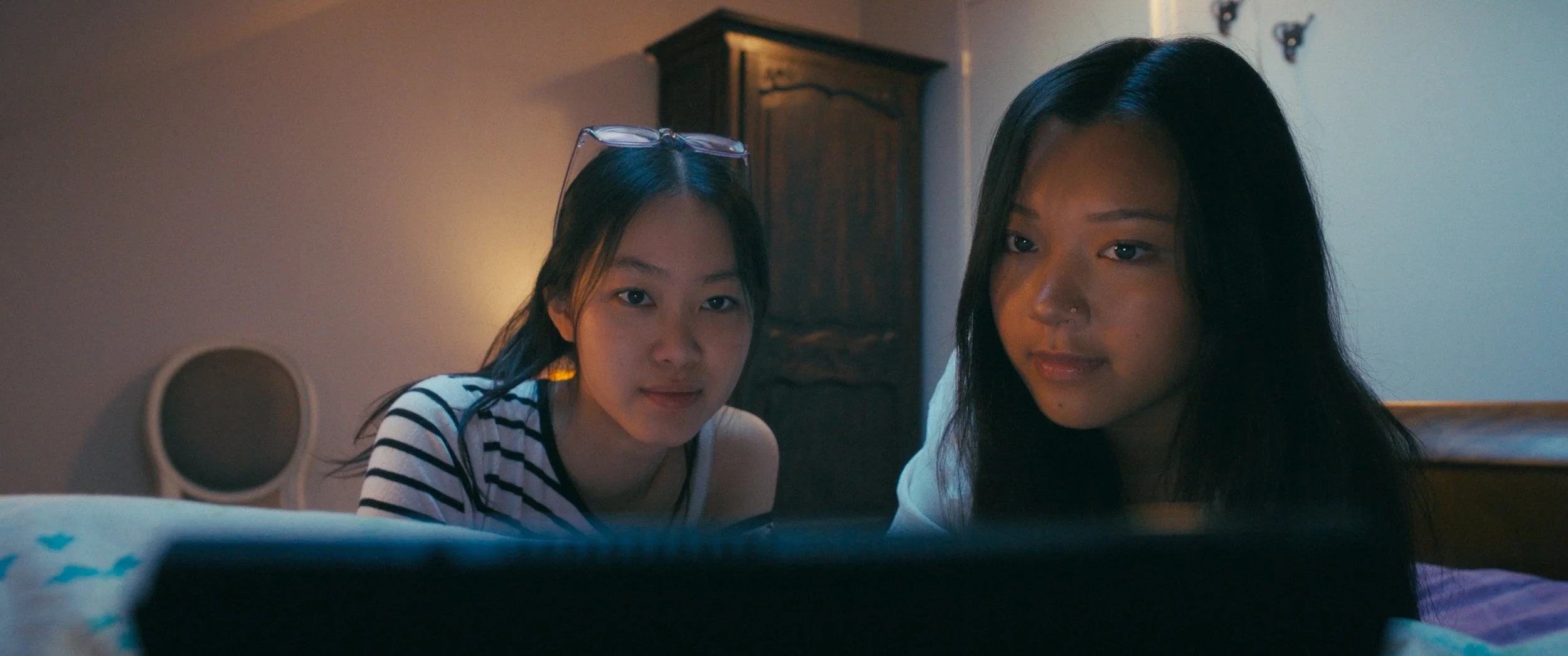 Two young women looking at a Switch playing in a dimly lit room