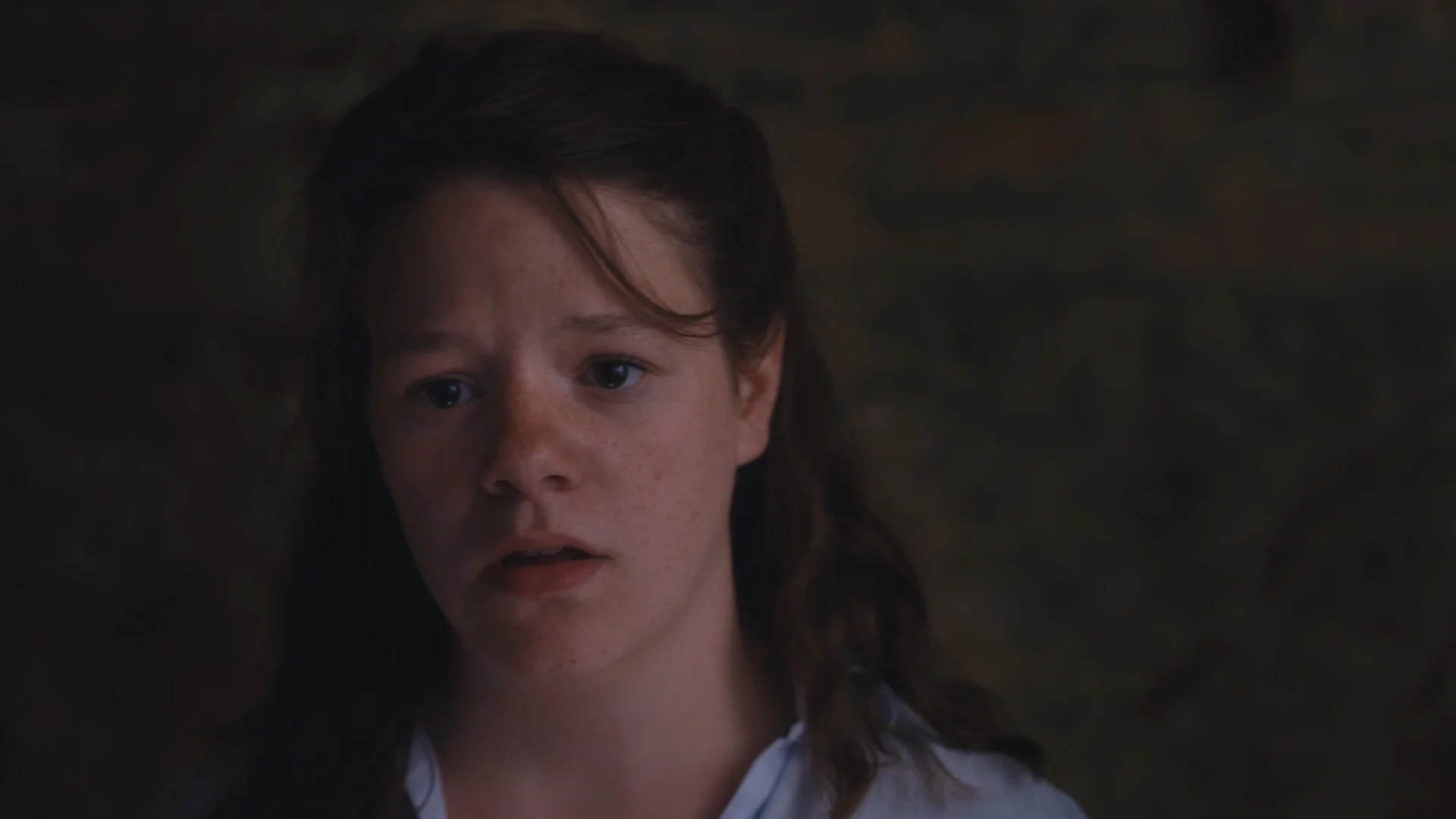 Close-up of a young woman with brown hair and freckles, looking upward with a worried or surprised expression.