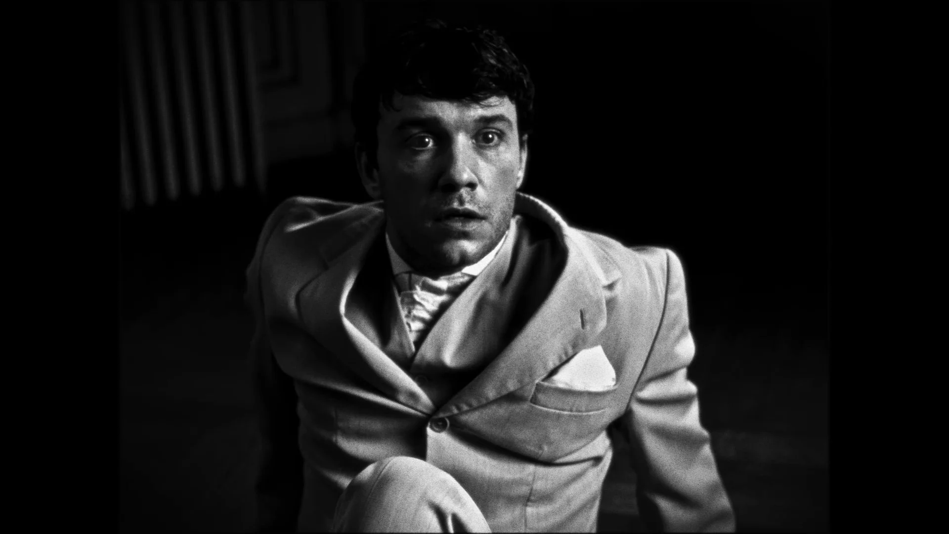 A black-and-white photo of a man in a suit, looking upward with a surprised or intense expression.