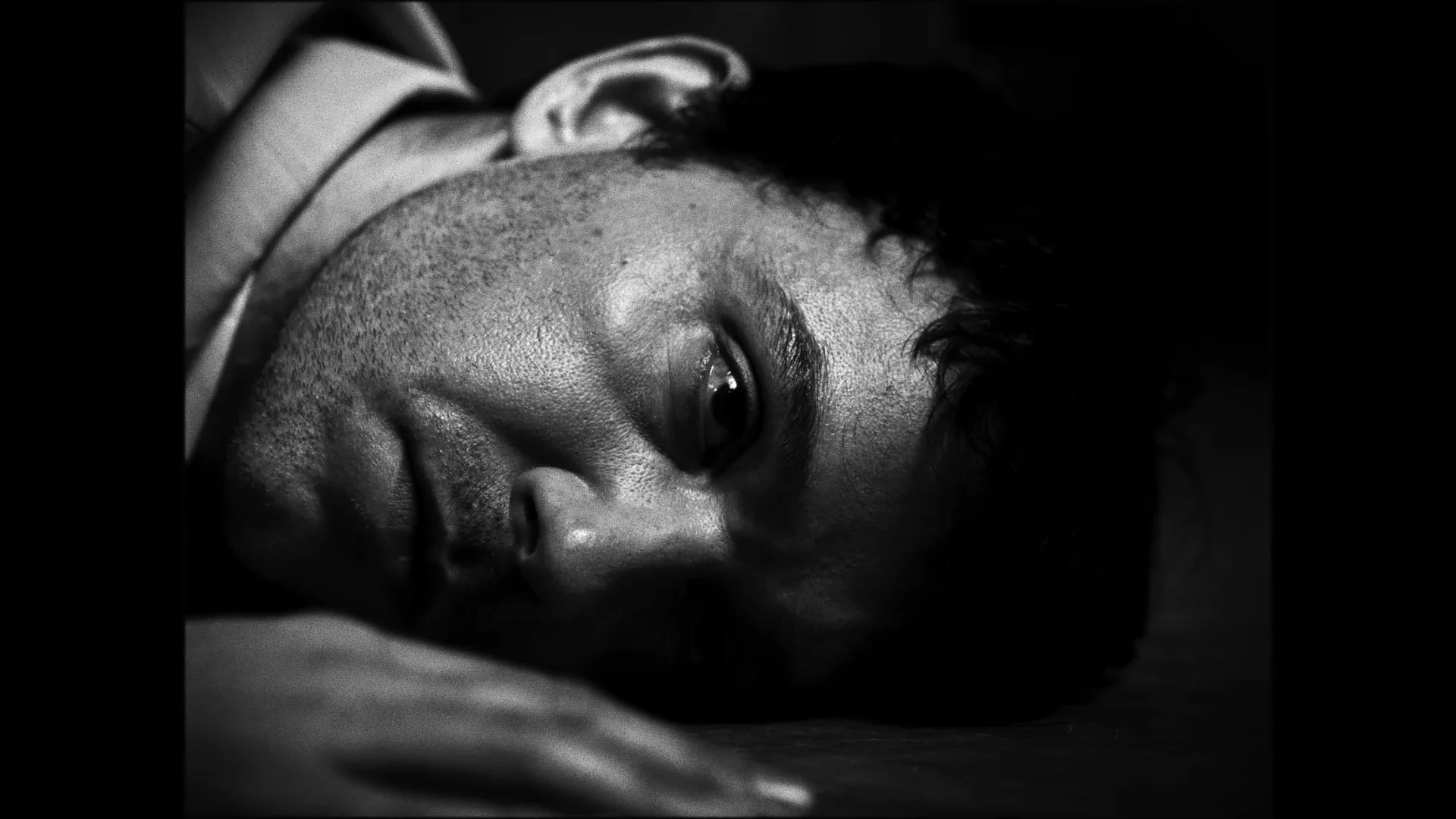 Close-up black and white photograph of a man lying on his side with his eyes open.