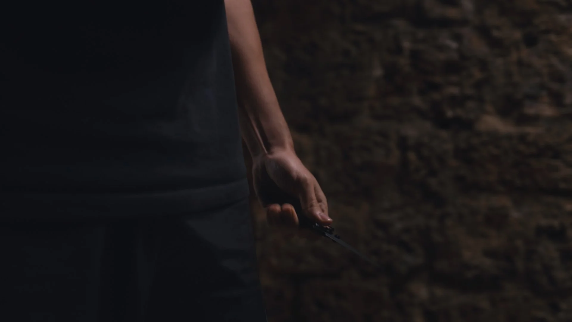 A person's hand holding a knife, visible from their waist to fingertips, against a dark background.