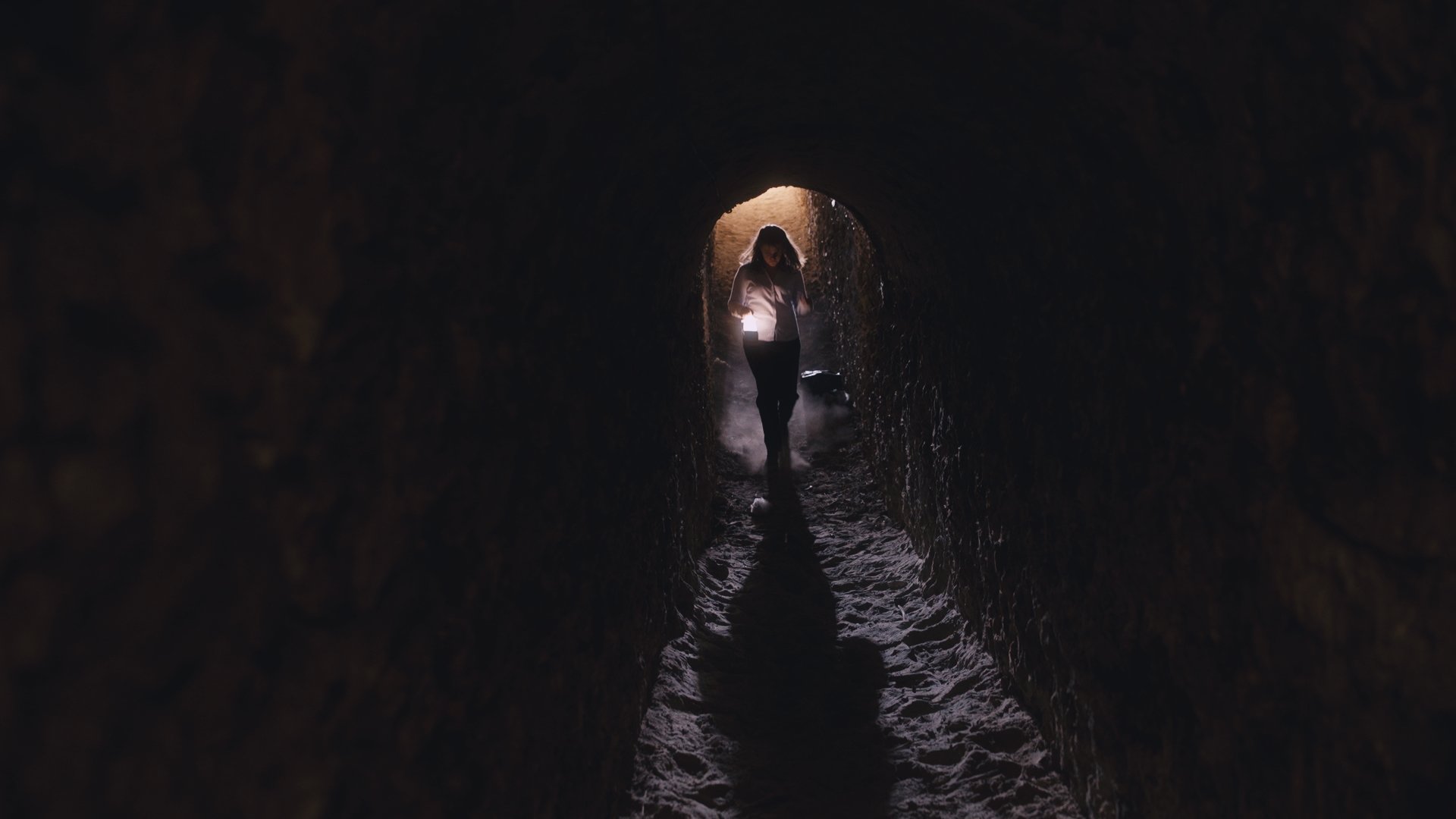 Person walking through a dark tunnel with light coming from the exit.