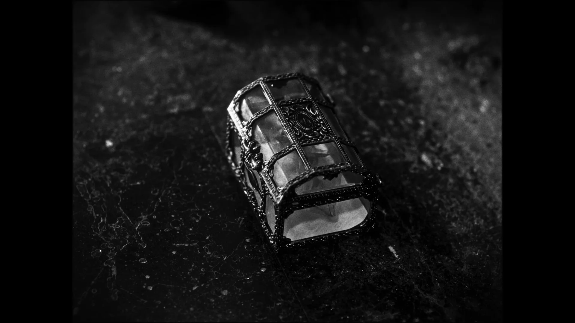 A vintage metal and glass lantern sitting on a dark textured surface in black and white.