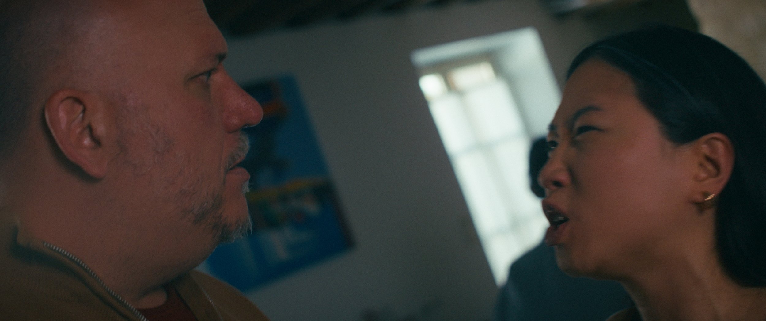 A tense confrontation between a man with a beard and a woman with dark hair in an indoor setting.