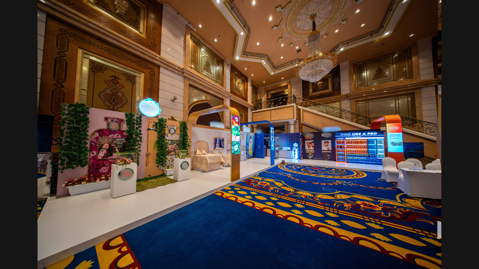 Interior of a luxurious hotel lobby with ornate ceiling, grand chandelier, and decorative walls. There are various vending machines and display booths, including a shave product stand, against a patterned carpet.