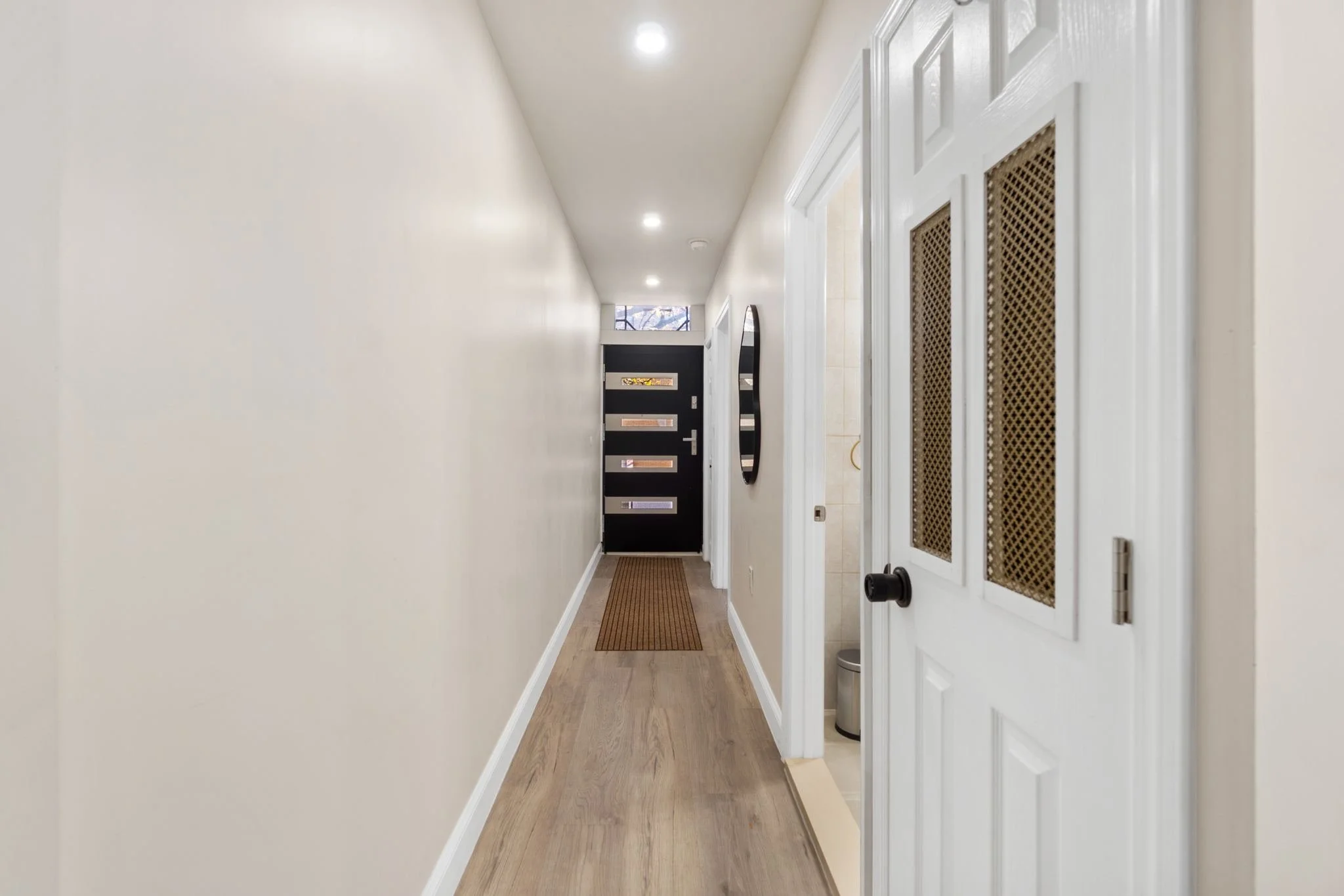 Hallway with white walls, wooden floor, and a door with a vent cover on the right side.