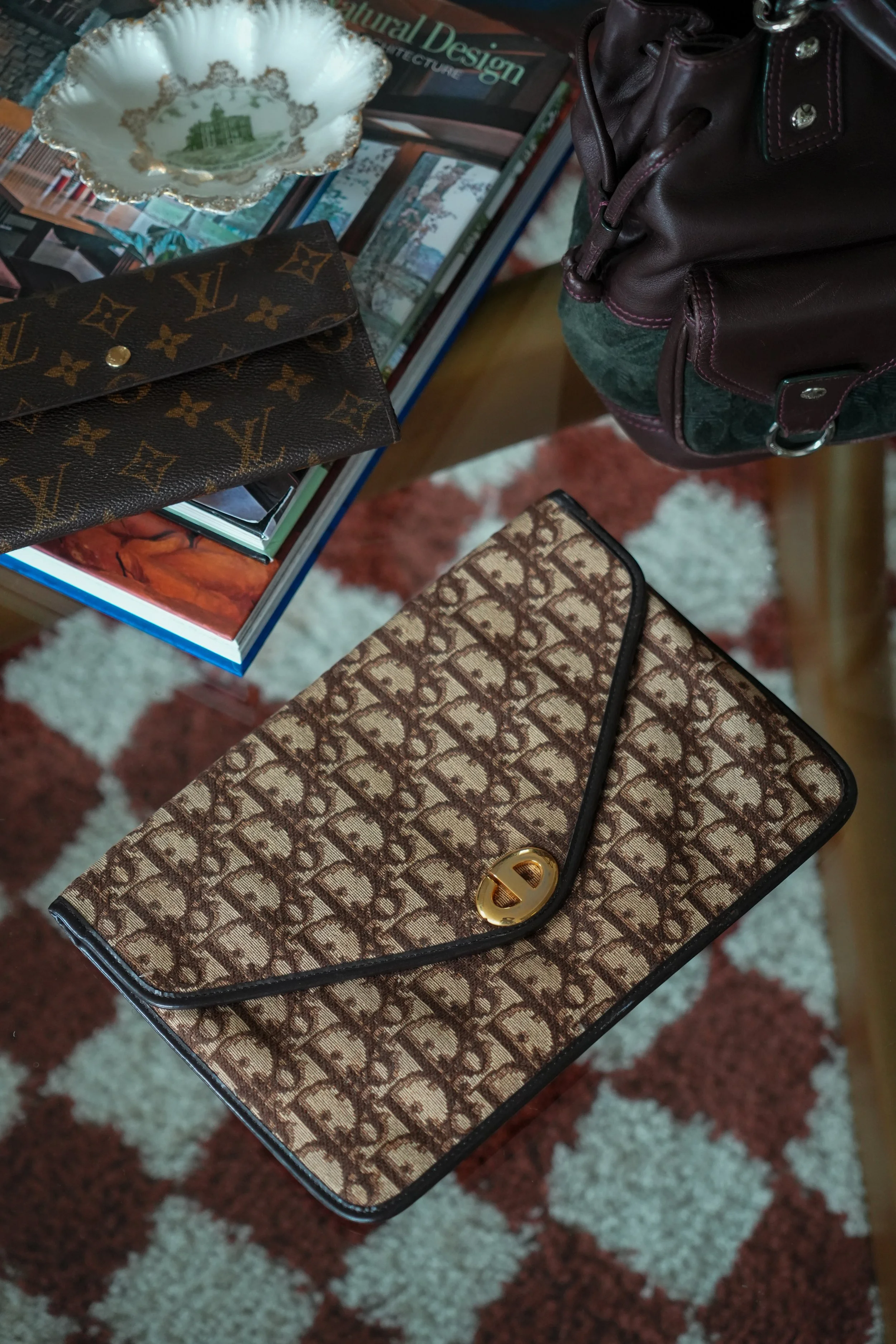 Close-up of several designer bags and jewelry on a table, with magazines and a decorative bowl in the background.