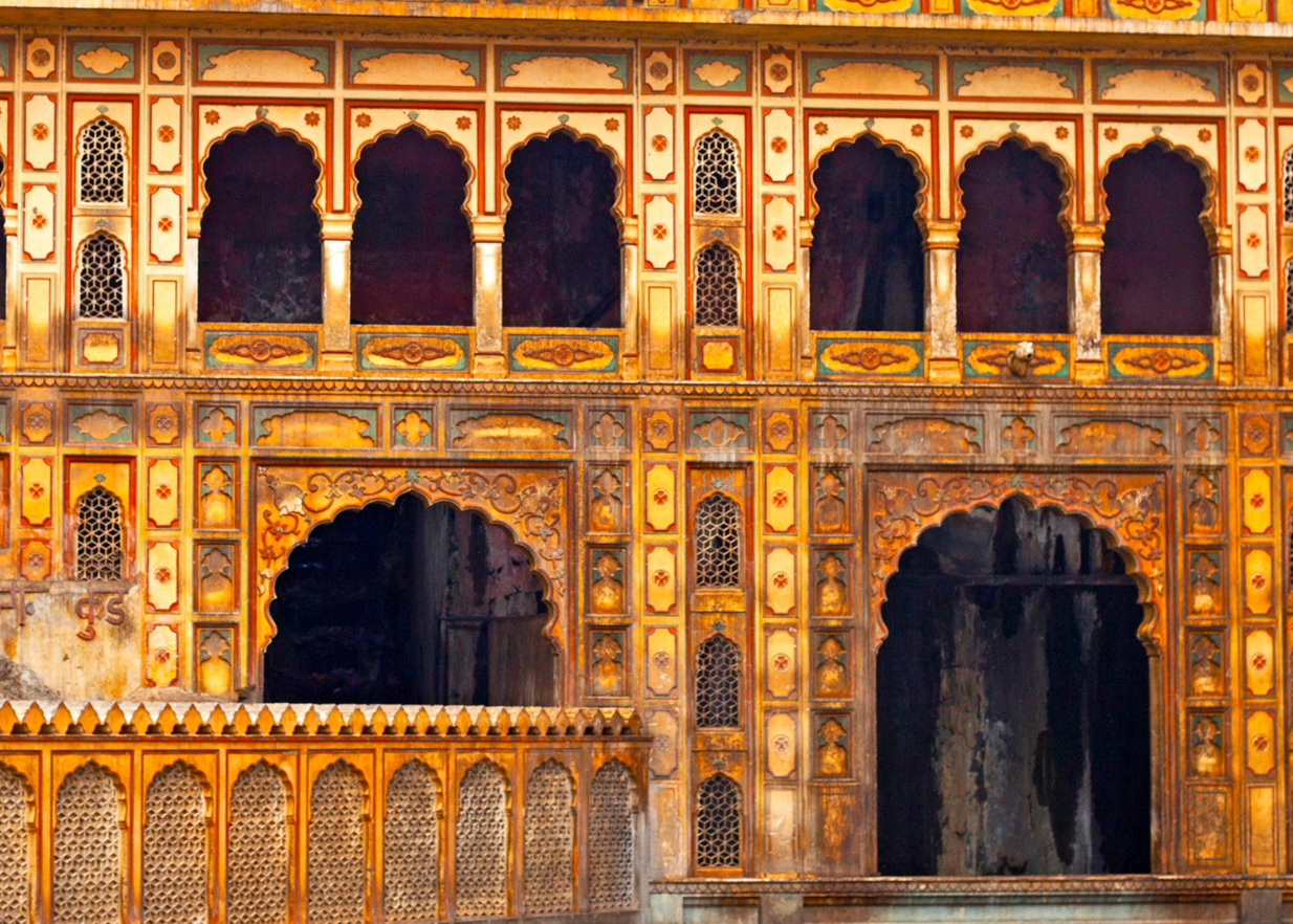 Close-up of an ornate, historical building facade with arched windows and intricate decorative patterns, painted in yellow, orange, and gold hues.