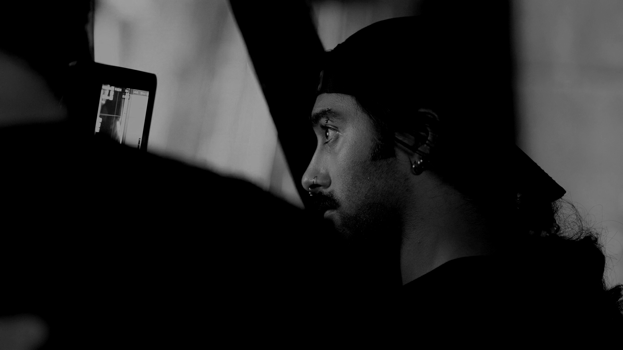 A person with piercings and a nose ring looking at a camera in a mirror in black and white.