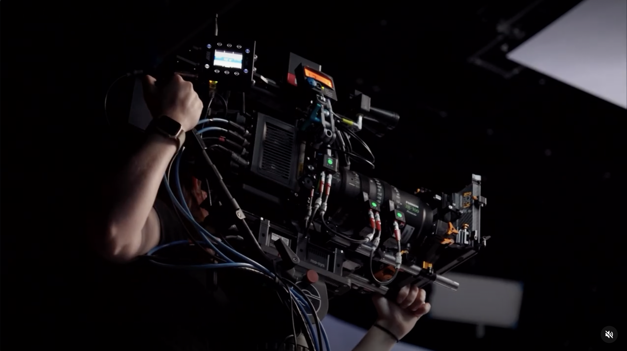 Close-up of a person operating a professional camera rig in a dark setting, with various electronic equipment and wires attached.