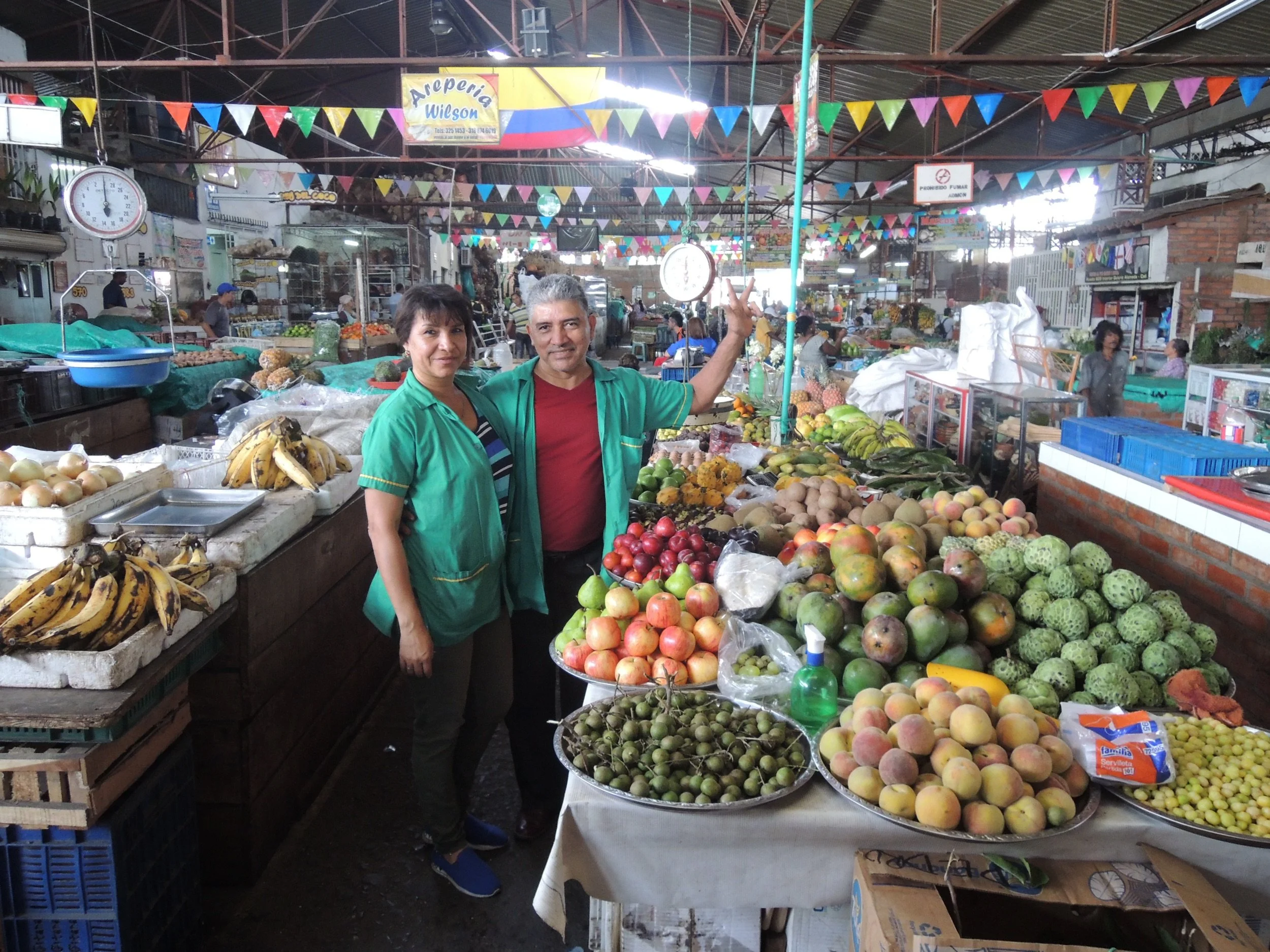 Vendors behind a colorful fruit stand at Alameda Market in Cali, Colombia.