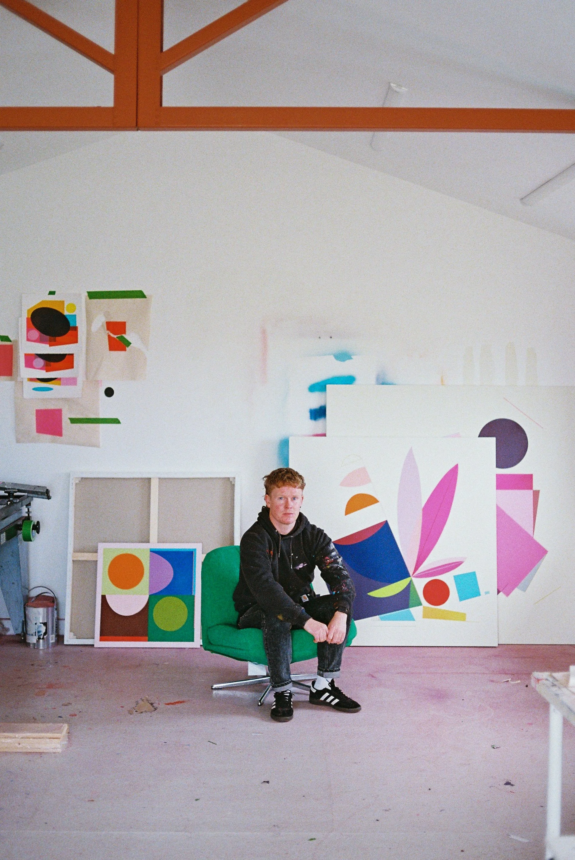 Irish contemporary artist Luke Reidy sitting in his art studio, surrounded by colourful abstract paintings and original artwork.