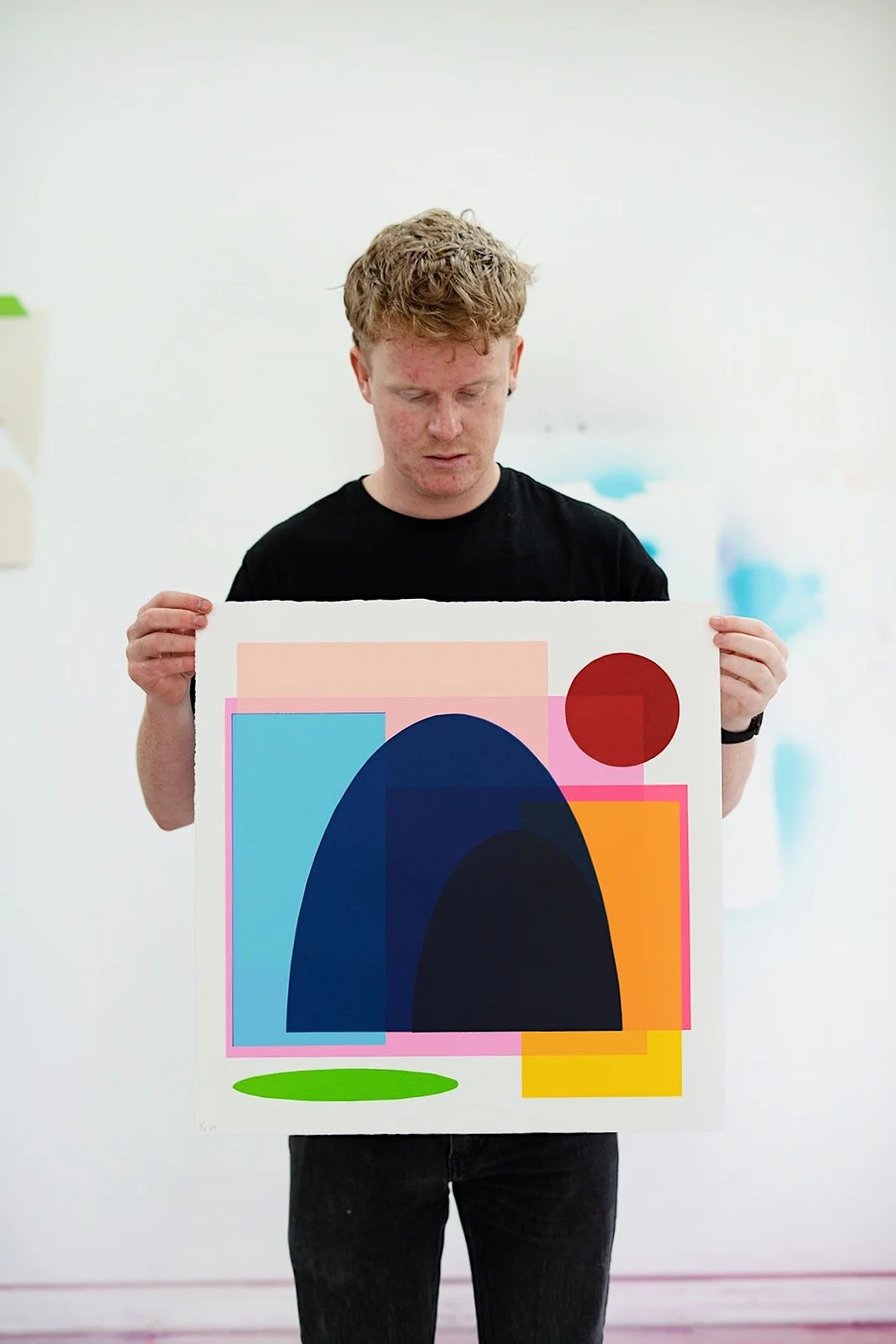 Artist Luke Reidy holding a colourful abstract screenprint