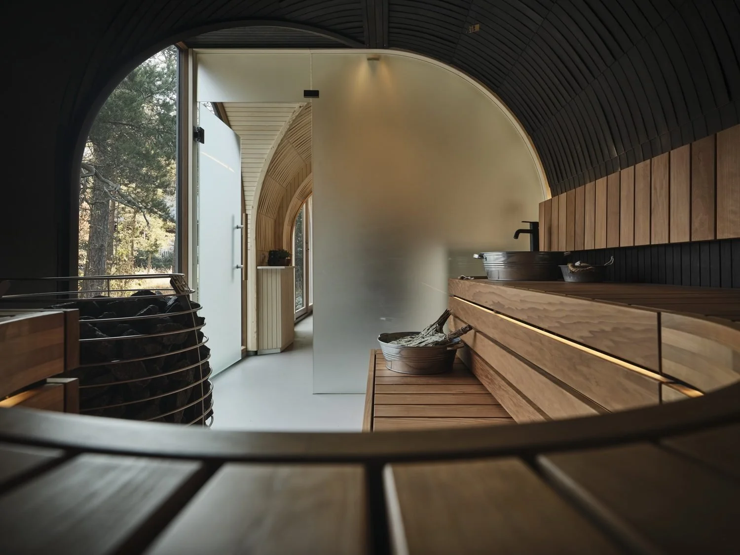 Inside the sauna, an arched glass window looking out at trees