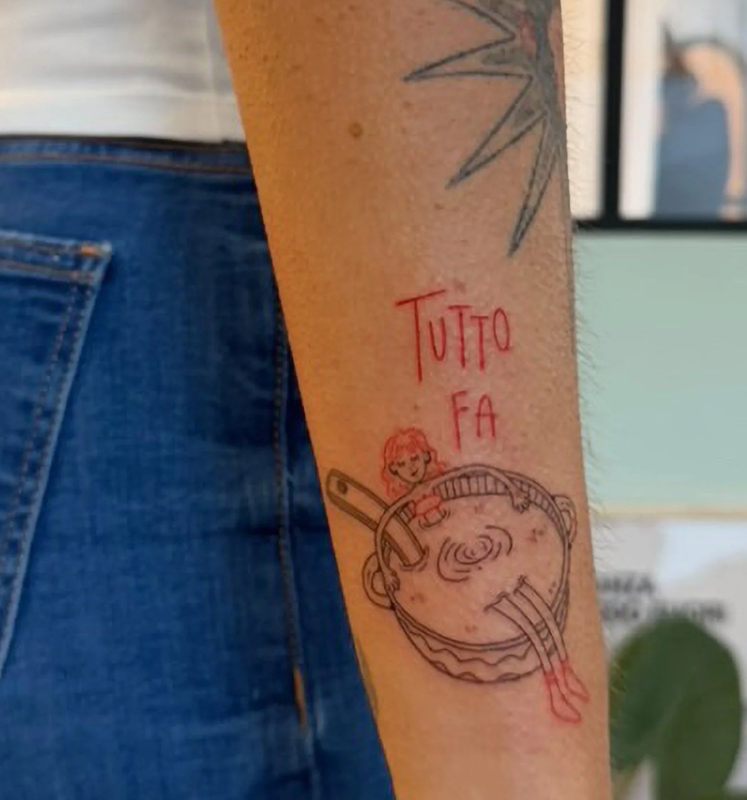 Tatuaggio sull'avambraccio con le parole "TUTTO FA" e disegni di una donna e un'onda.