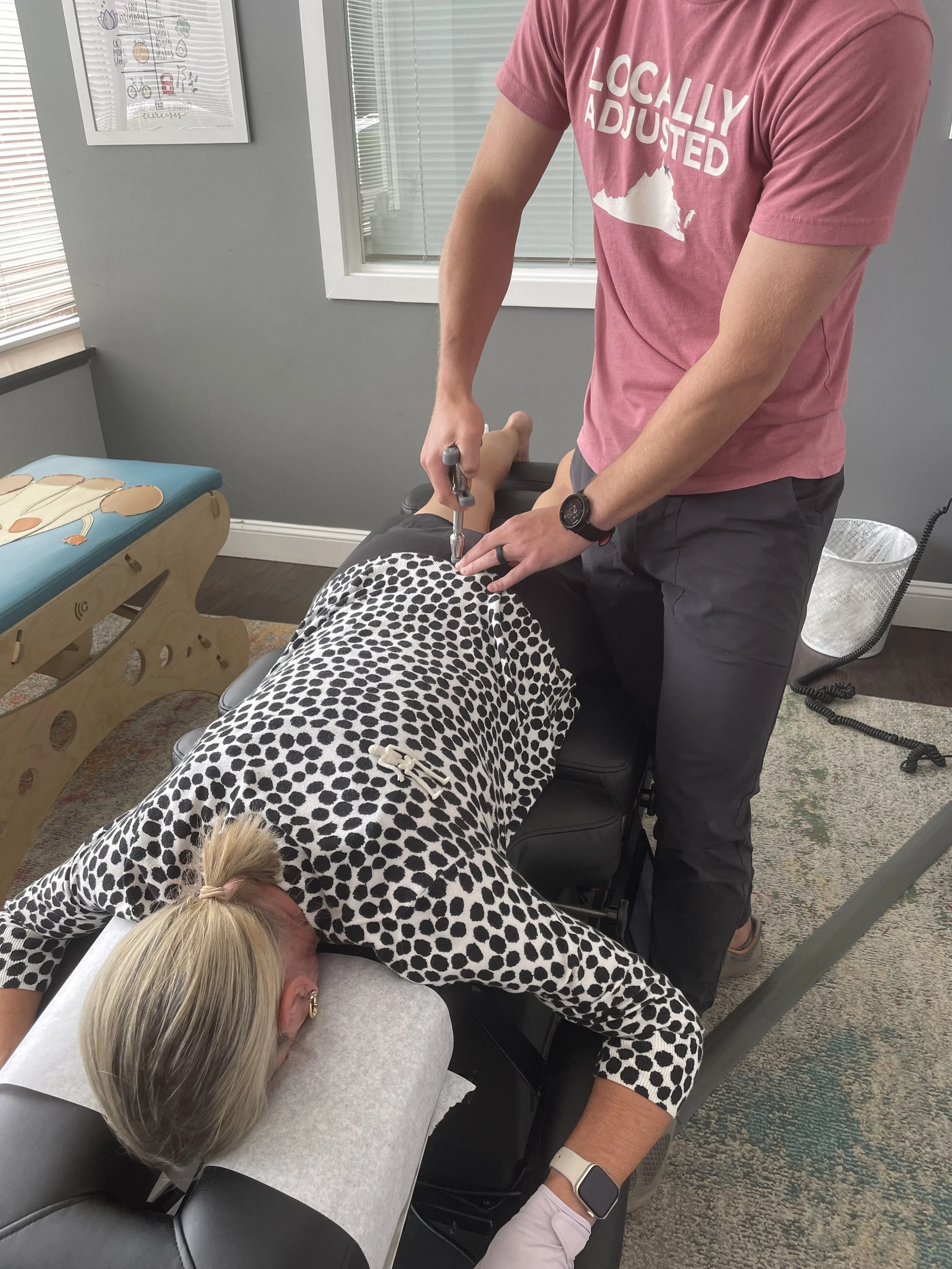 A woman receiving acupuncture treatment while lying face down on a treatment table, with her face resting in a cushioned face cradle, and a practitioner inserting acupuncture needles into her back.